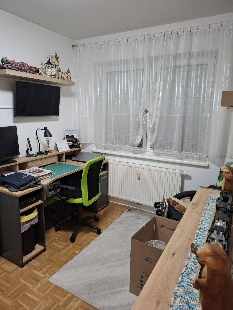 Arbeitszimmer mit Schreibtisch, Computer und einem großen Fenster mit Vorhängen.