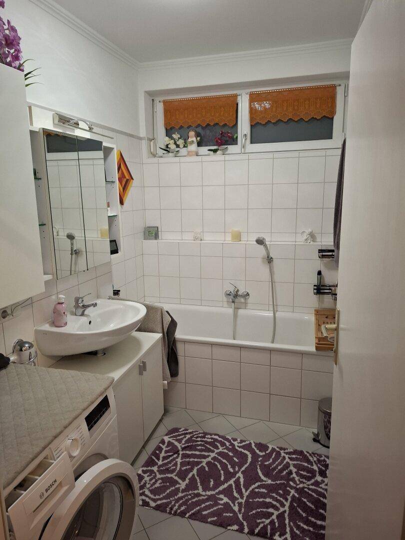Badezimmer mit Badewanne, Waschbecken, Waschmaschine und weißen Fliesen.