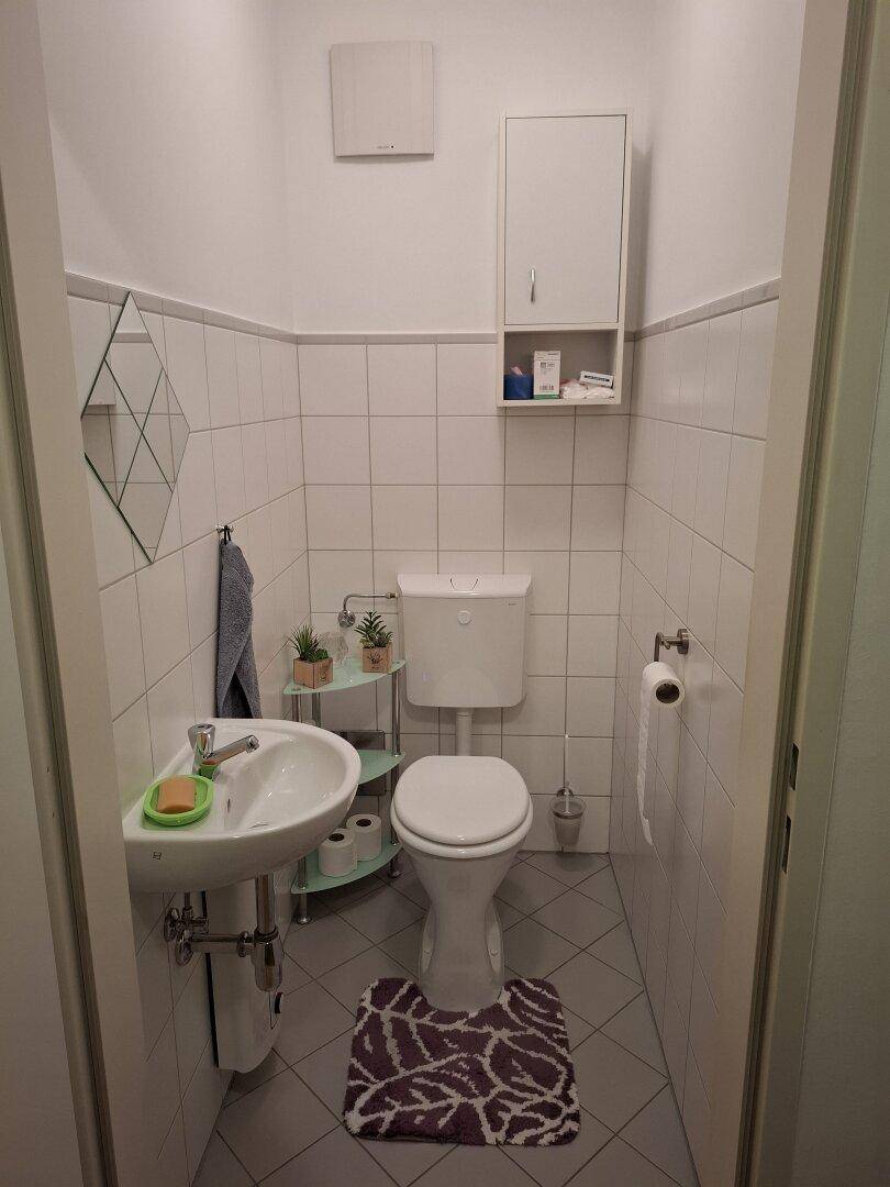 Kleines Gäste-WC mit Toilette, Waschbecken und weißen Fliesen an Wänden und Boden.