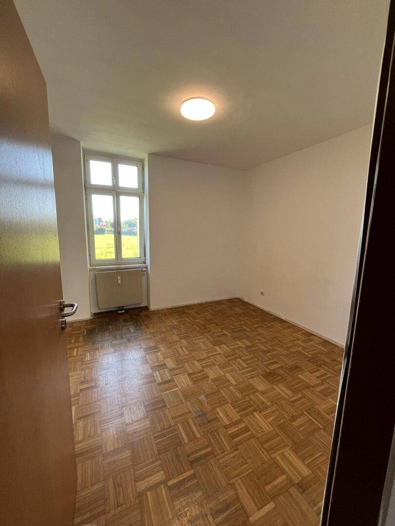 Geräumiges Schlafzimmer mit Parkettboden und Fenster mit Blick ins Grüne, bietet viel Tageslicht.