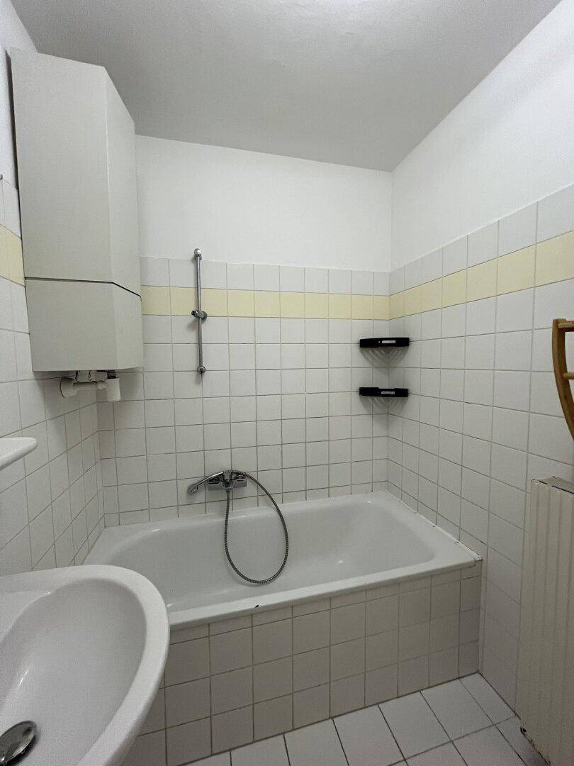 Badezimmer mit Badewanne, Waschbecken und weißen Fliesen im klassischen 80er-Jahre-Stil.