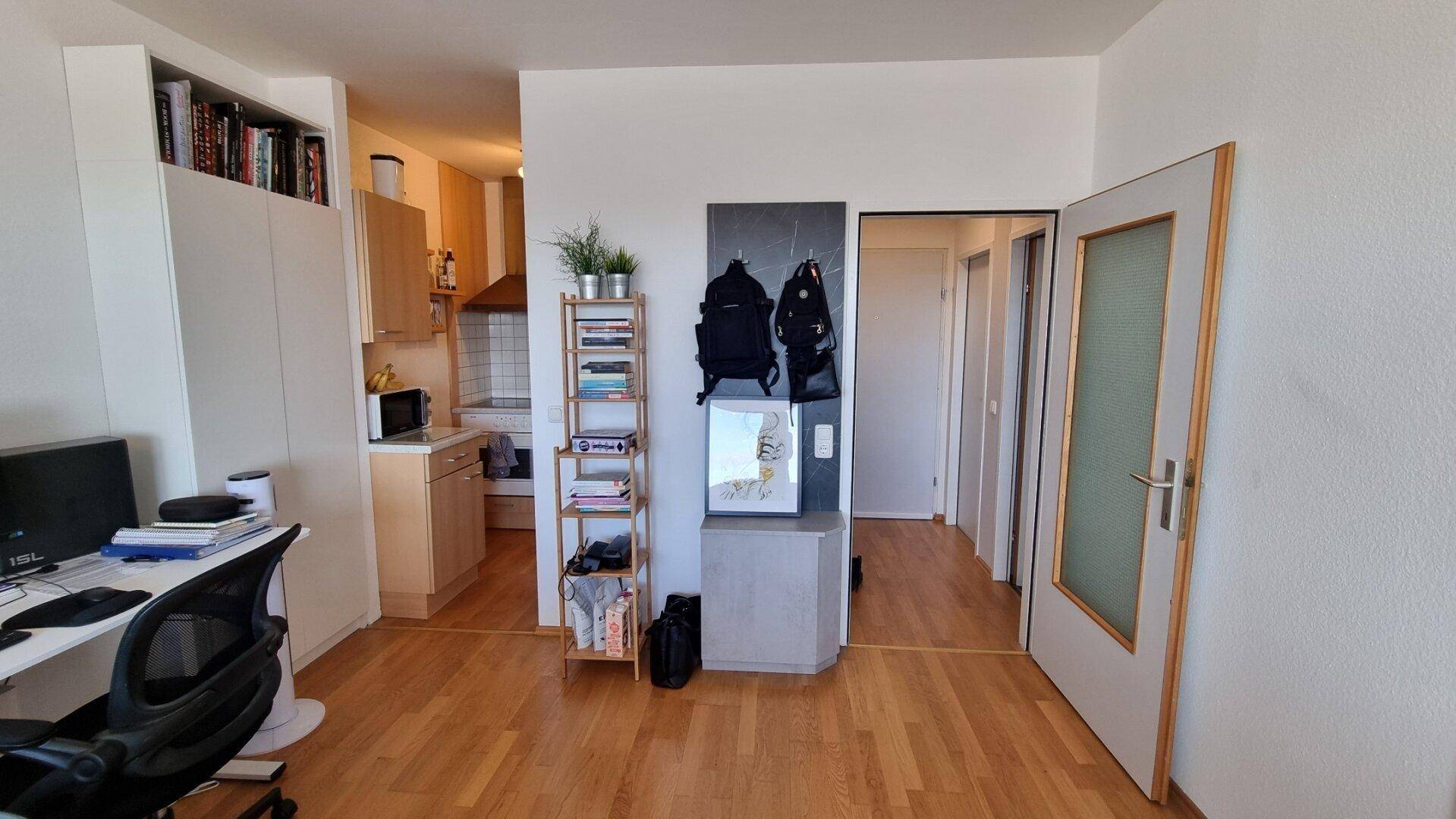 Offener Wohnbereich mit Arbeitsplatz, Blick zur Küche und Zugang zum Flur.