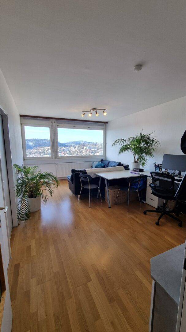 Heller Wohn- und Essbereich mit Holzboden, großem Fenster und Stadtblick.