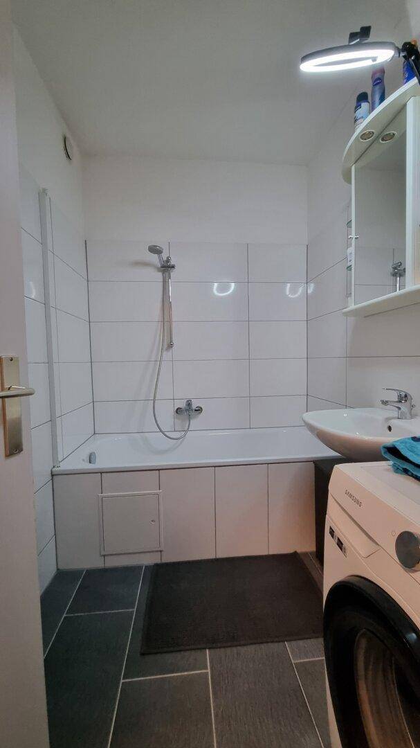 Badezimmer mit Badewanne, Duschfunktion, Waschbecken und Waschmaschine.