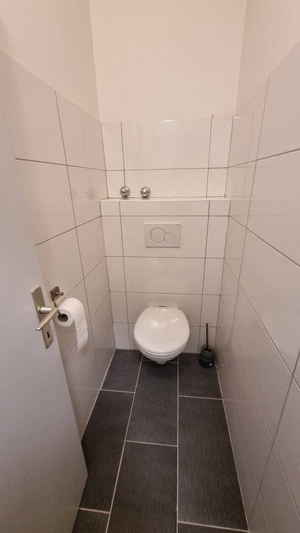 Separates WC mit Wandtoilette und Fliesenboden in neutralen Farben.