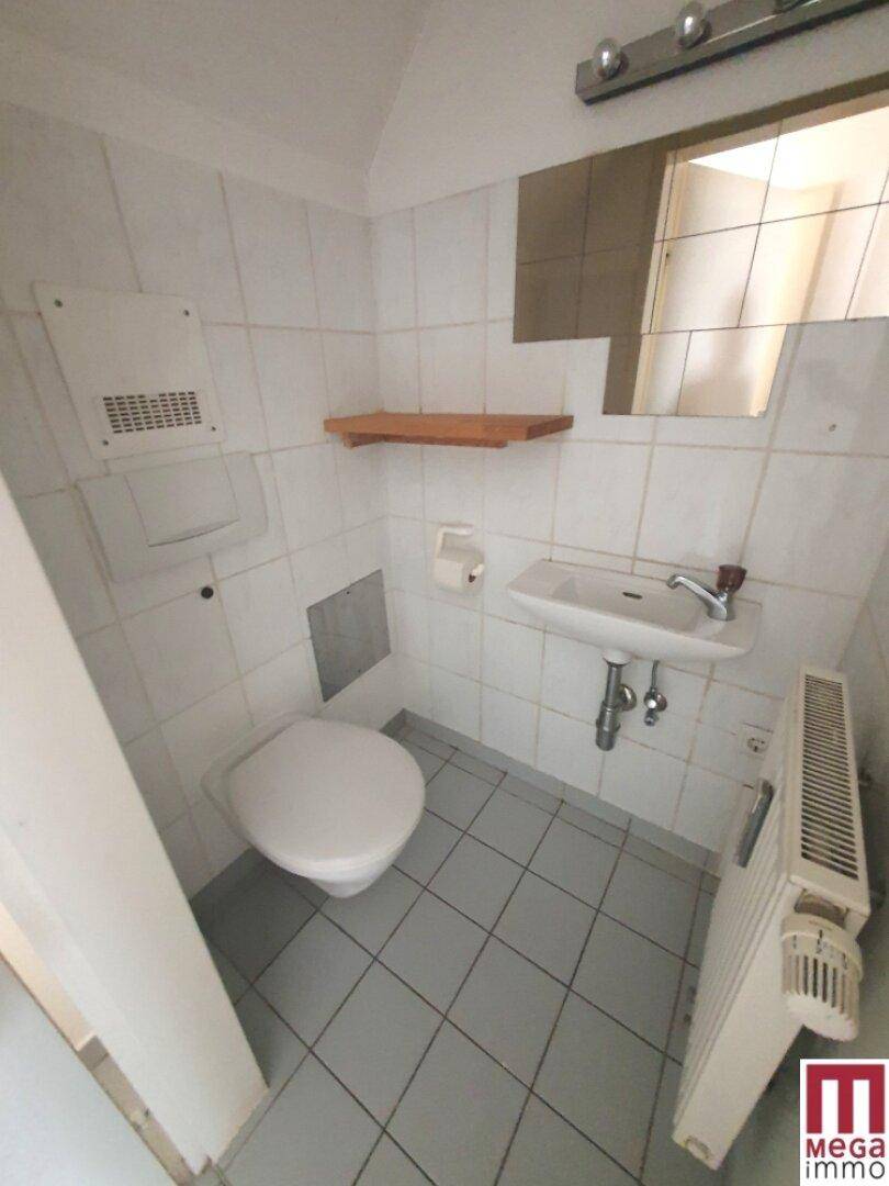 Kleiner Toilettenraum mit weißen Fliesen, WC, Waschbecken und Heizkörper, funktional und sauber.