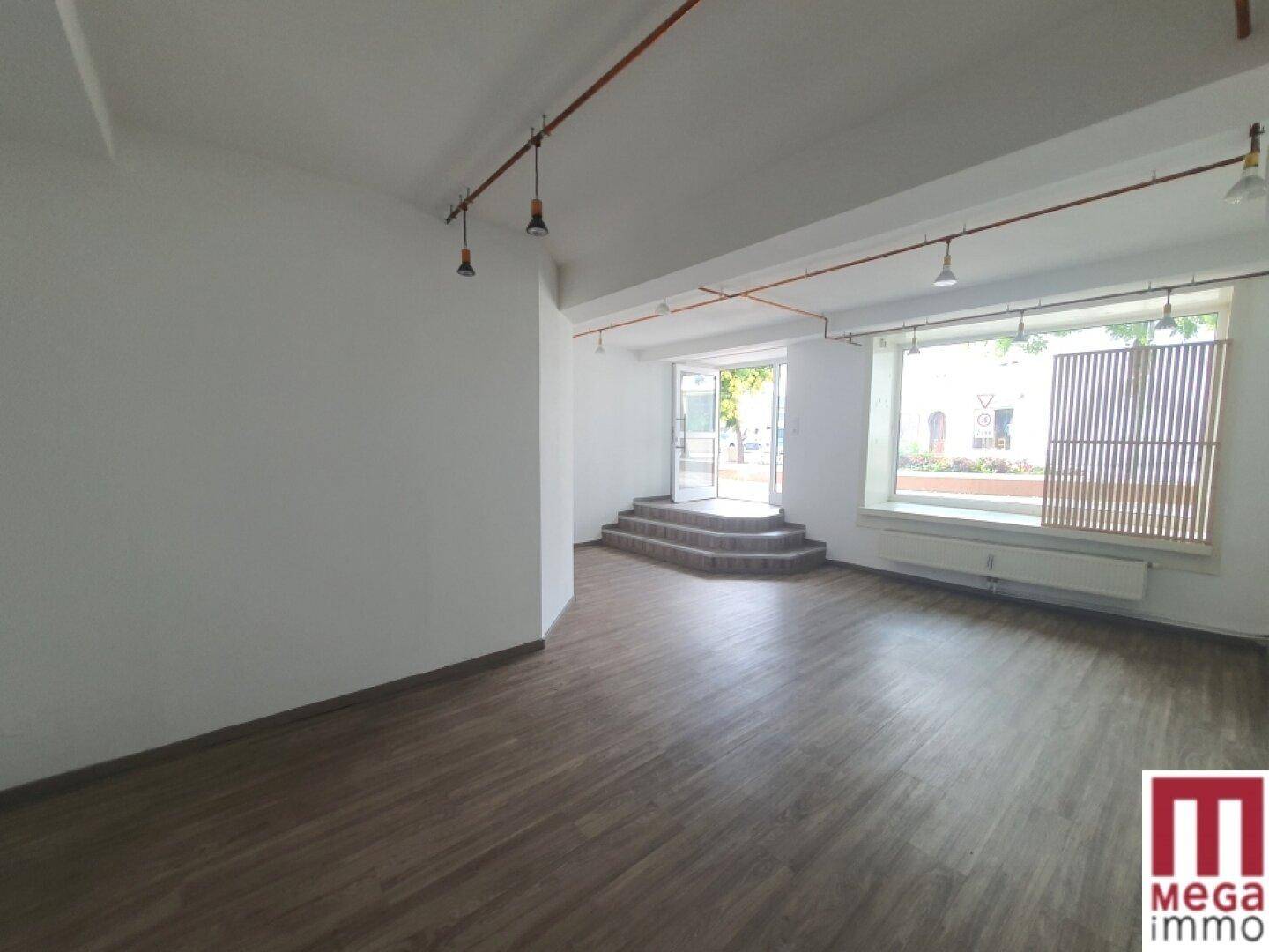 Heller Geschäftsraum mit Stufen zum Eingang, großen Fenstern und Holzoptik-Boden, ideal für ein Ladenlokal.