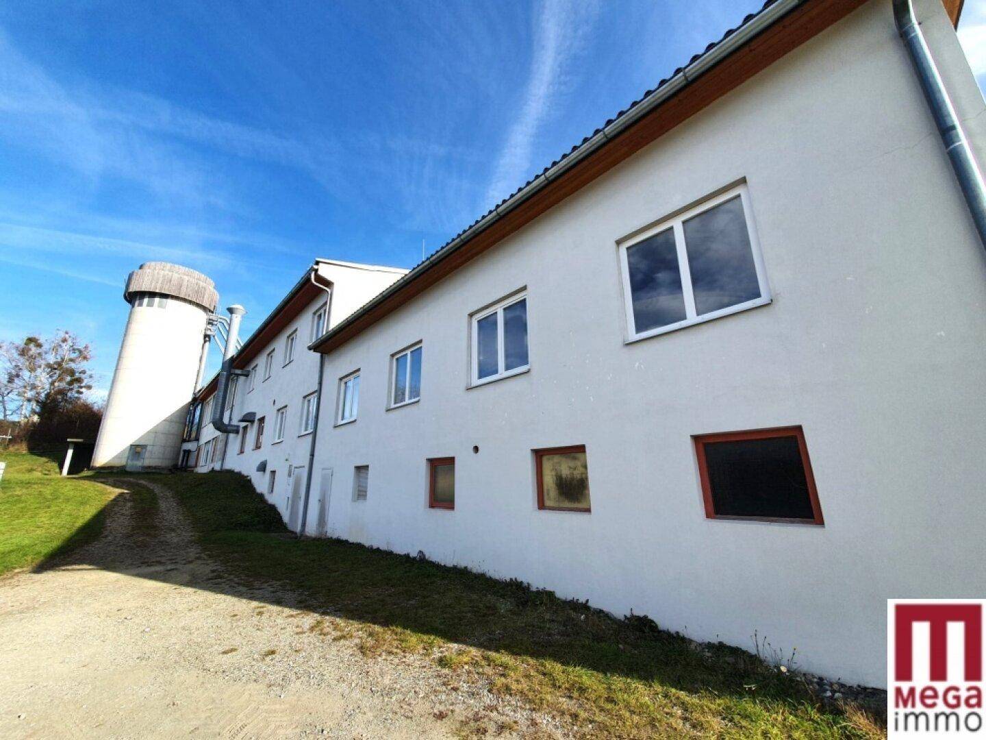 Lange Seitenfassade des Gebäudes mit vielen Fenstern und einem runden Turm im Hintergrund.