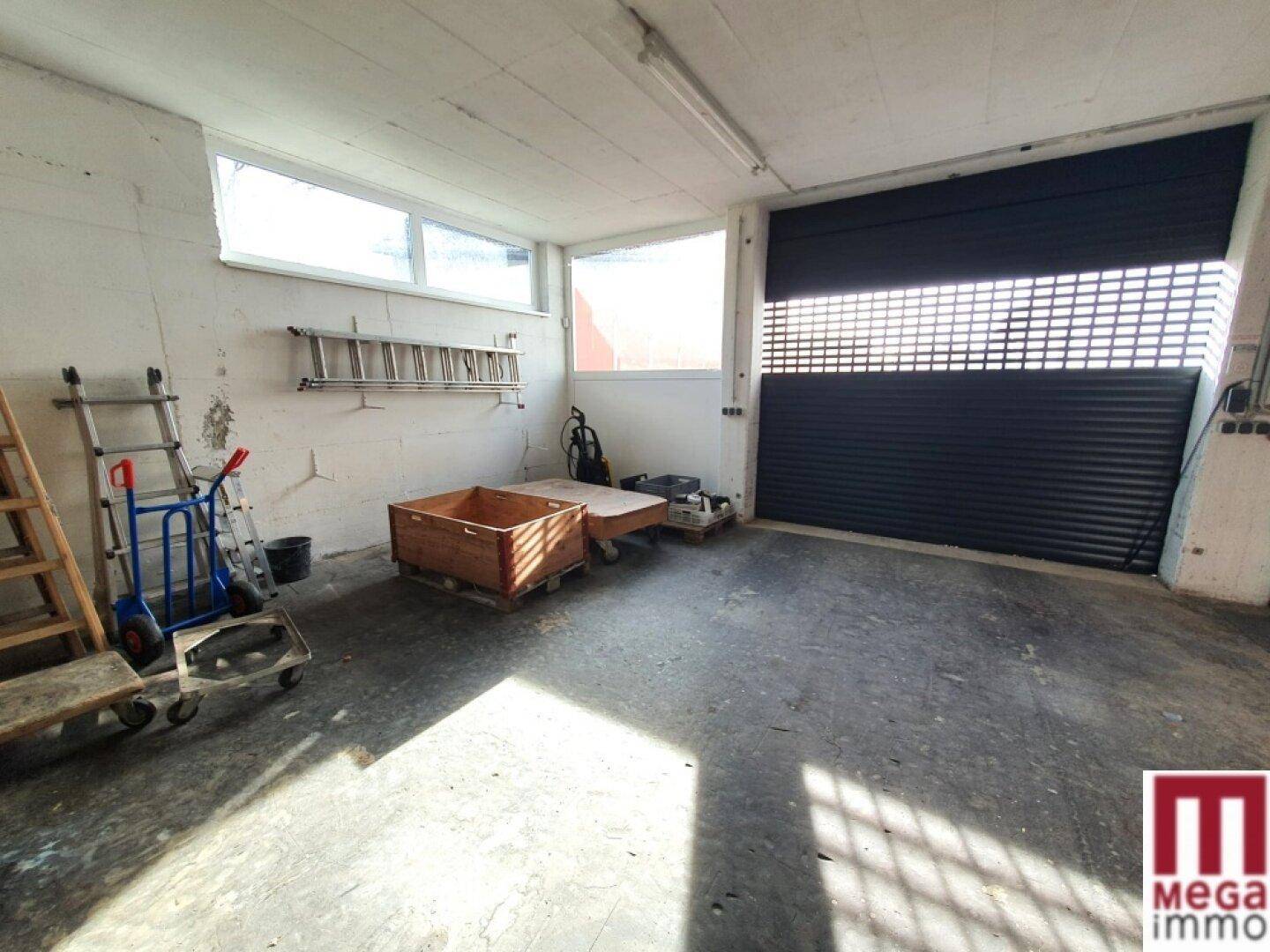 Werkstatt oder Lagerraum mit Rolltor, Betonboden und verschiedenen Werkzeugen.