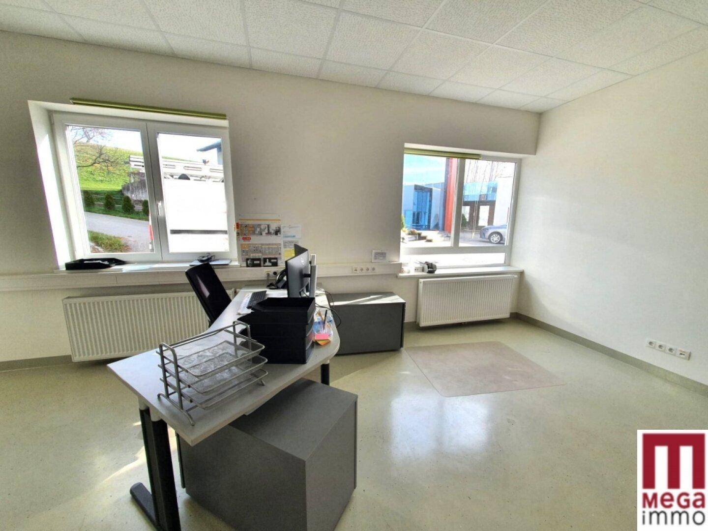 Helles Büro mit Schreibtisch, Heizkörpern und Fenstern mit Blick nach draußen.