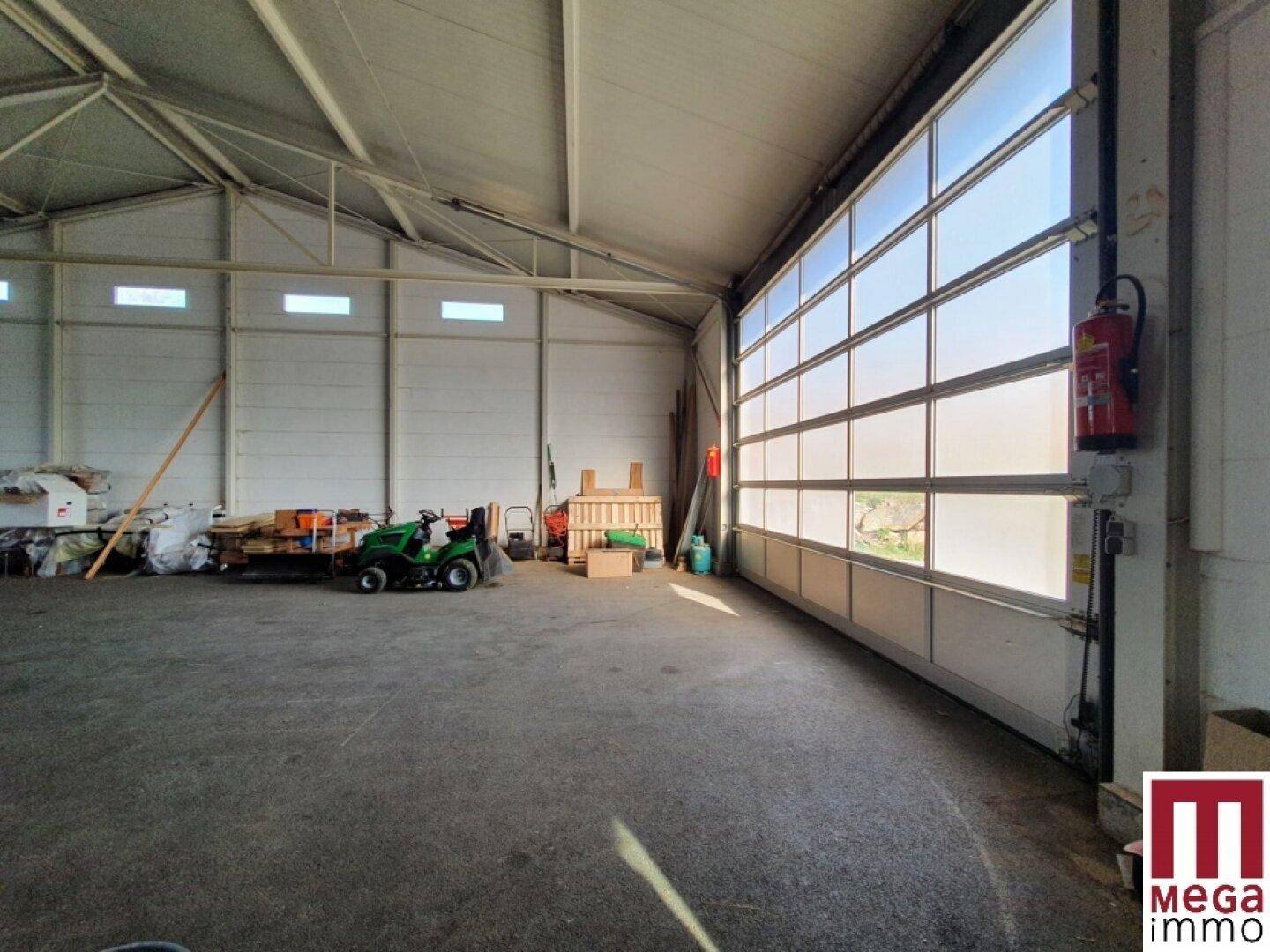 Große Lagerhalle mit Rolltor, Betonboden und viel Tageslicht durch die Fenster.