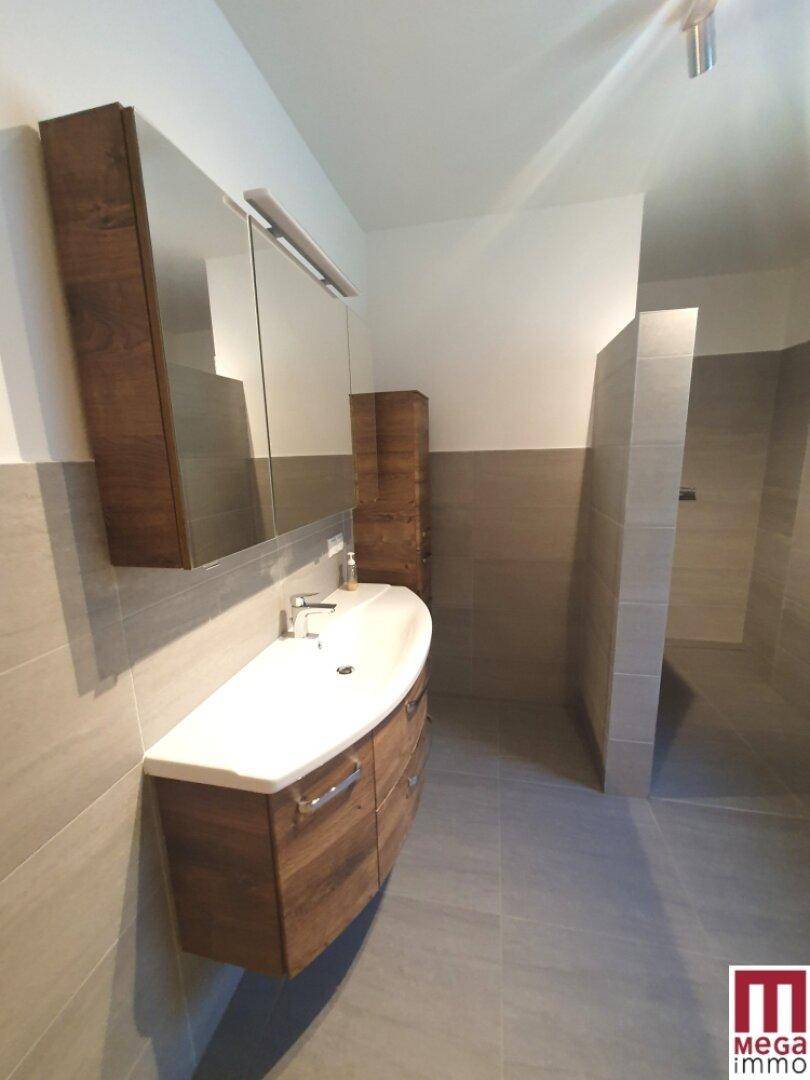 Badezimmer mit Holzwaschtisch, Spiegelschrank und begehbarer Dusche.
