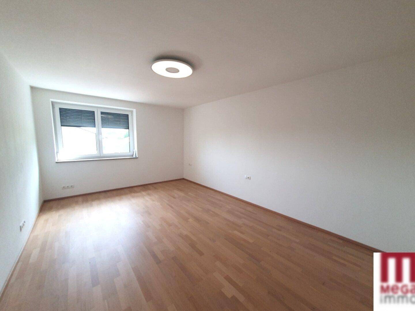 Helles Schlafzimmer mit Laminatboden und Fenster mit Rollladen.