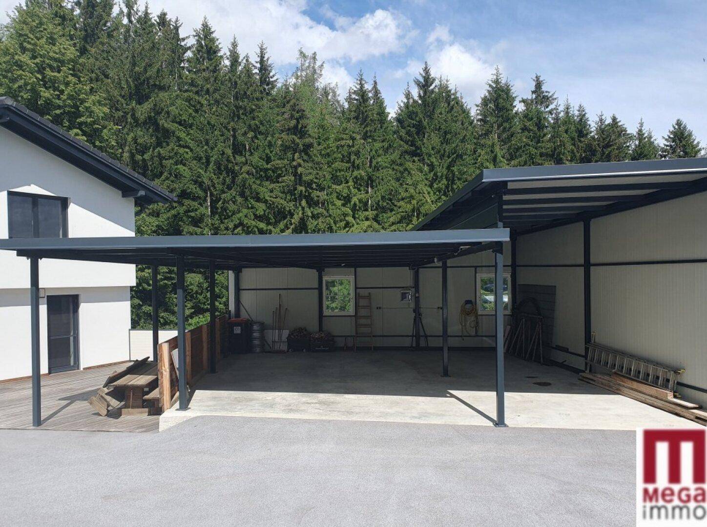 Modernes Haus mit großem Carport und überdachtem Parkbereich, umgeben von Wald.
