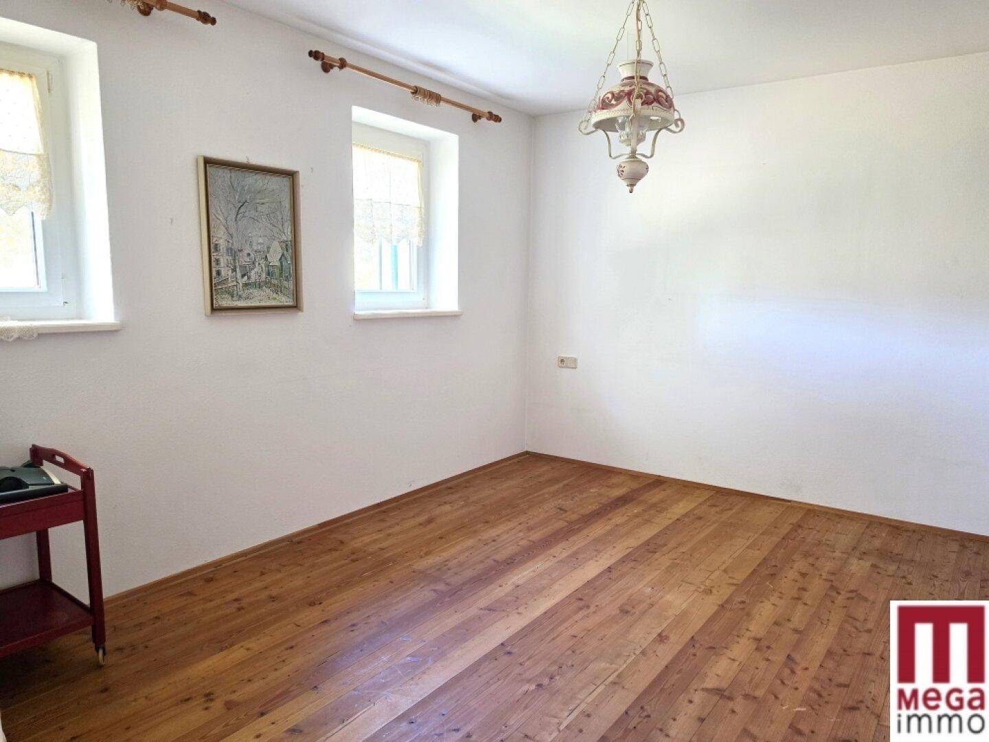 Leeres Zimmer mit Holzboden, weißen Wänden und zwei Fenstern, bereit zur individuellen Gestaltung.