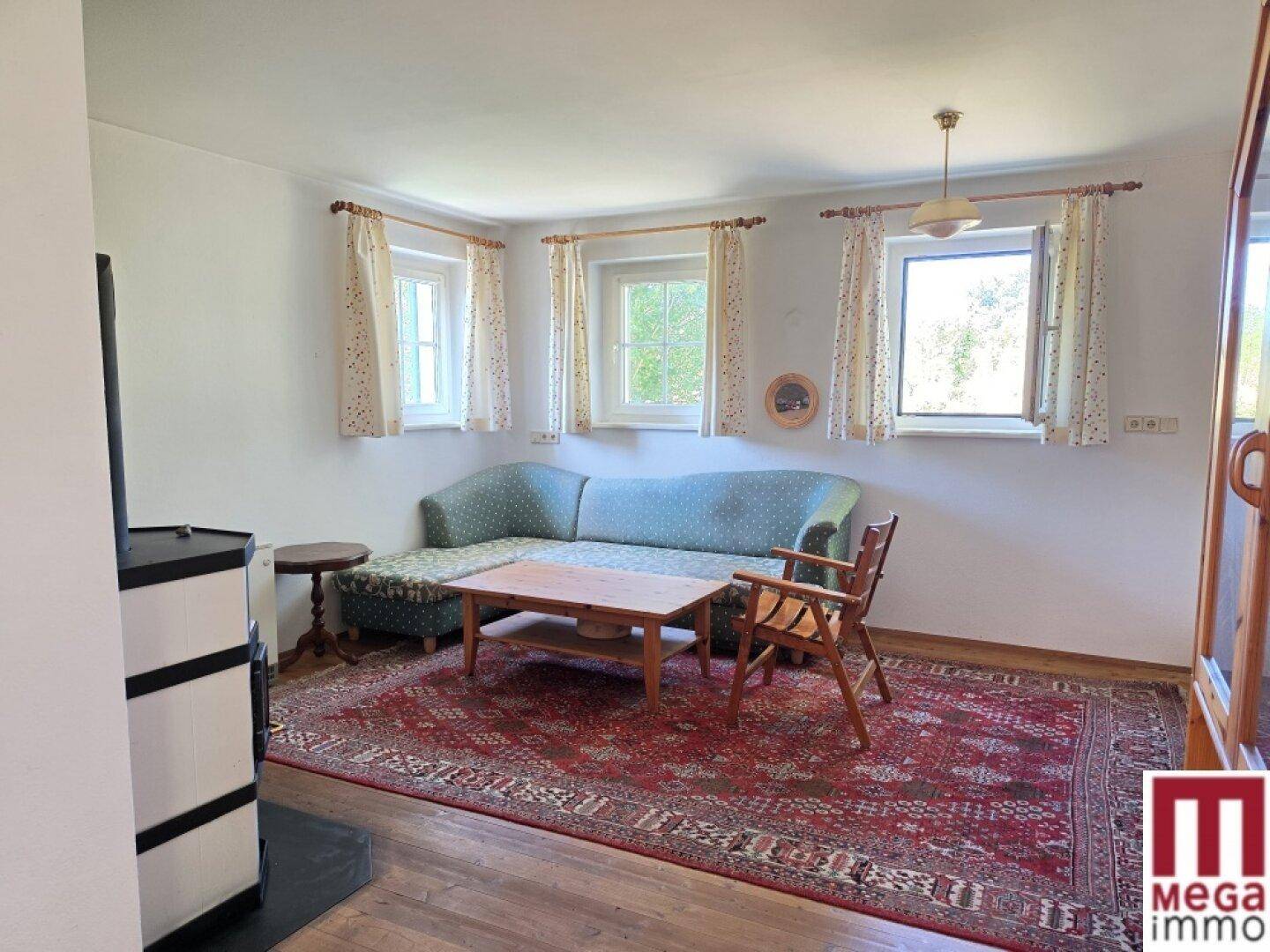 Gemütliches Wohnzimmer mit Sofa, Couchtisch, Teppich und mehreren Fenstern für viel Tageslicht.