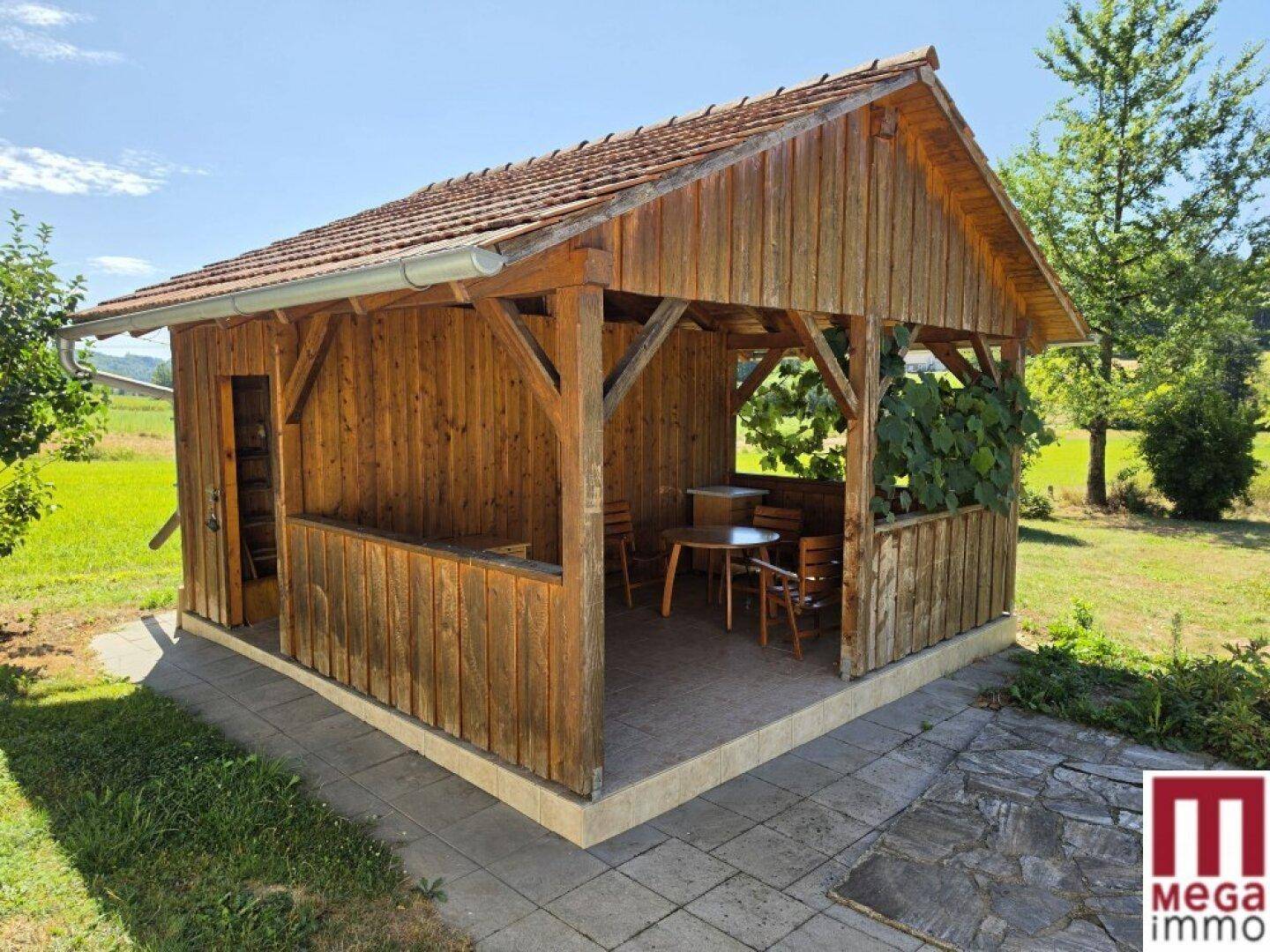 Gemütlicher Holzpavillon mit Ziegeldach und Sitzgelegenheiten im Grünen, ideal für Entspannung.
