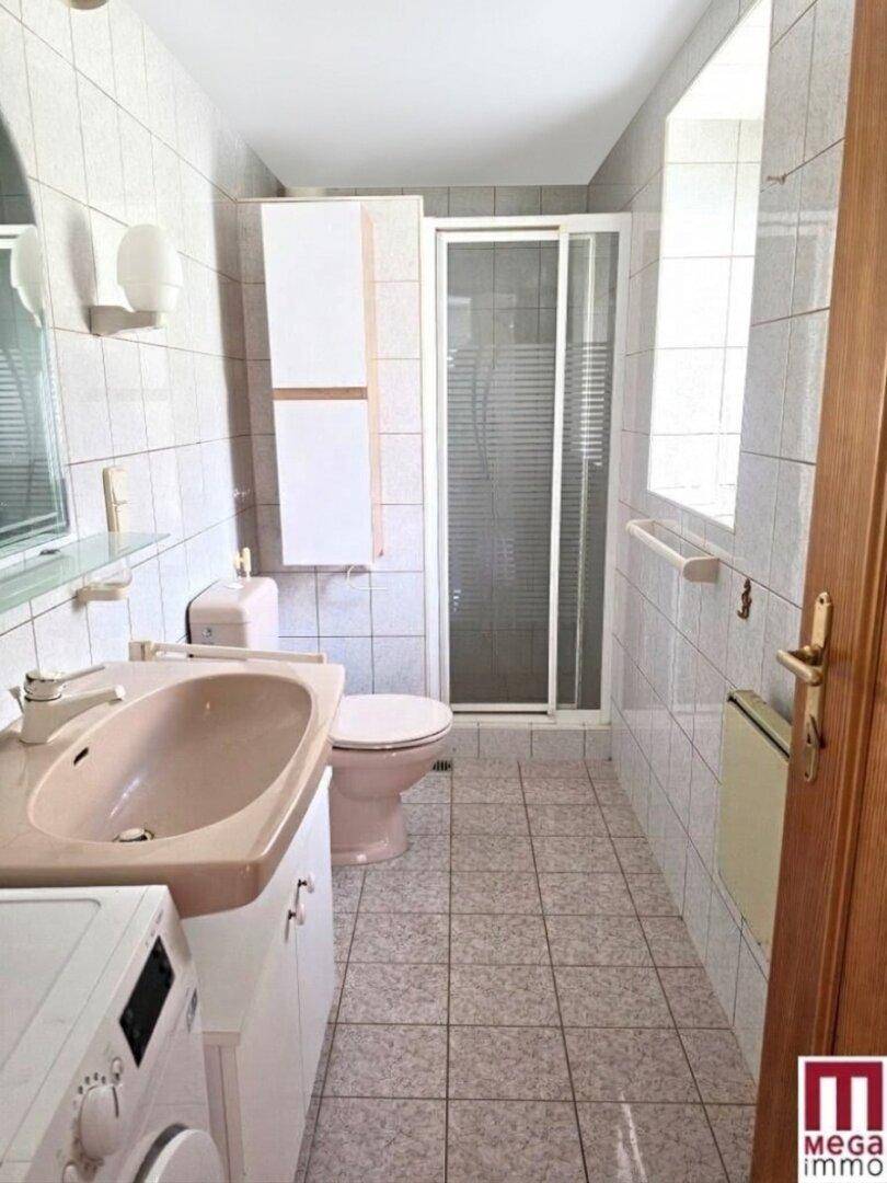 Badezimmer mit hellrosa Sanitärobjekten, Duschkabine, Fliesenboden und Waschmaschine.
