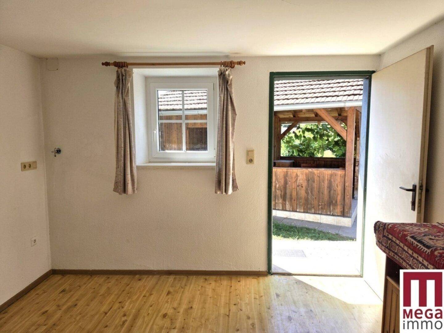 Heller Raum mit Holzboden und Fenster, mit direktem Zugang zu einem überdachten Außenbereich.