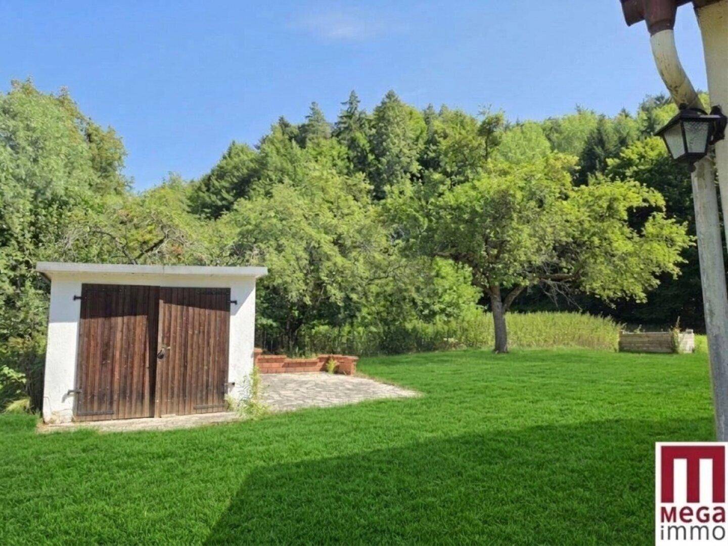 Großer, gepflegter Garten mit Rasenfläche, einem kleinen Schuppen und altem Baumbestand.