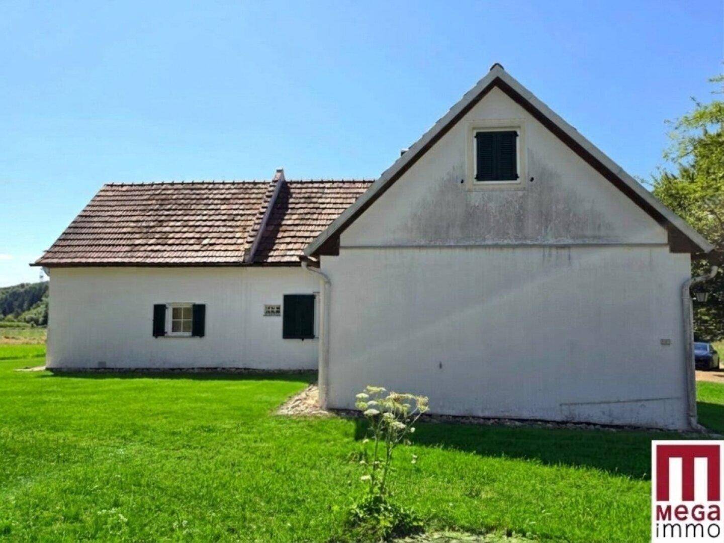 Seitenansicht des Hauses mit weißer Fassade, Ziegeldach und traditionellen grünen Fensterläden.
