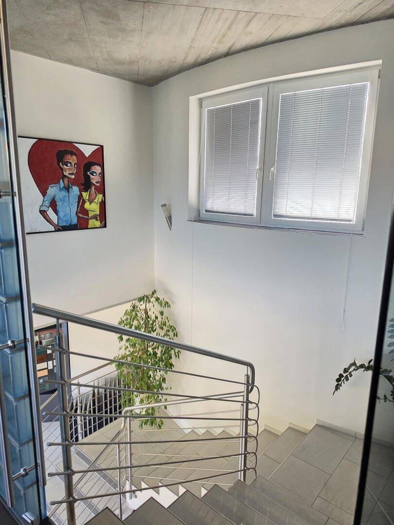 Treppenhaus mit modernen Metallgeländern, Fliesenboden und einem Fenster, das Tageslicht hereinlässt.