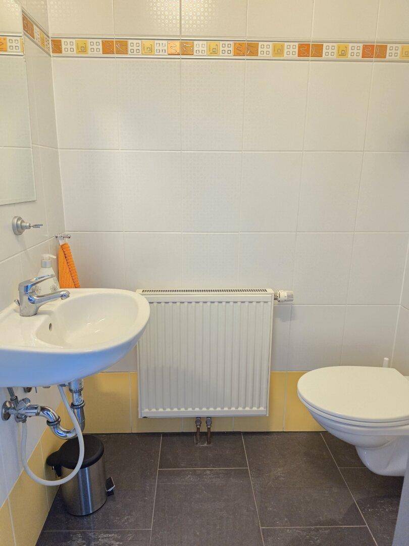 Gästetoilette mit Waschbecken, WC, Heizkörper und weiß-orange gefliesten Wänden.