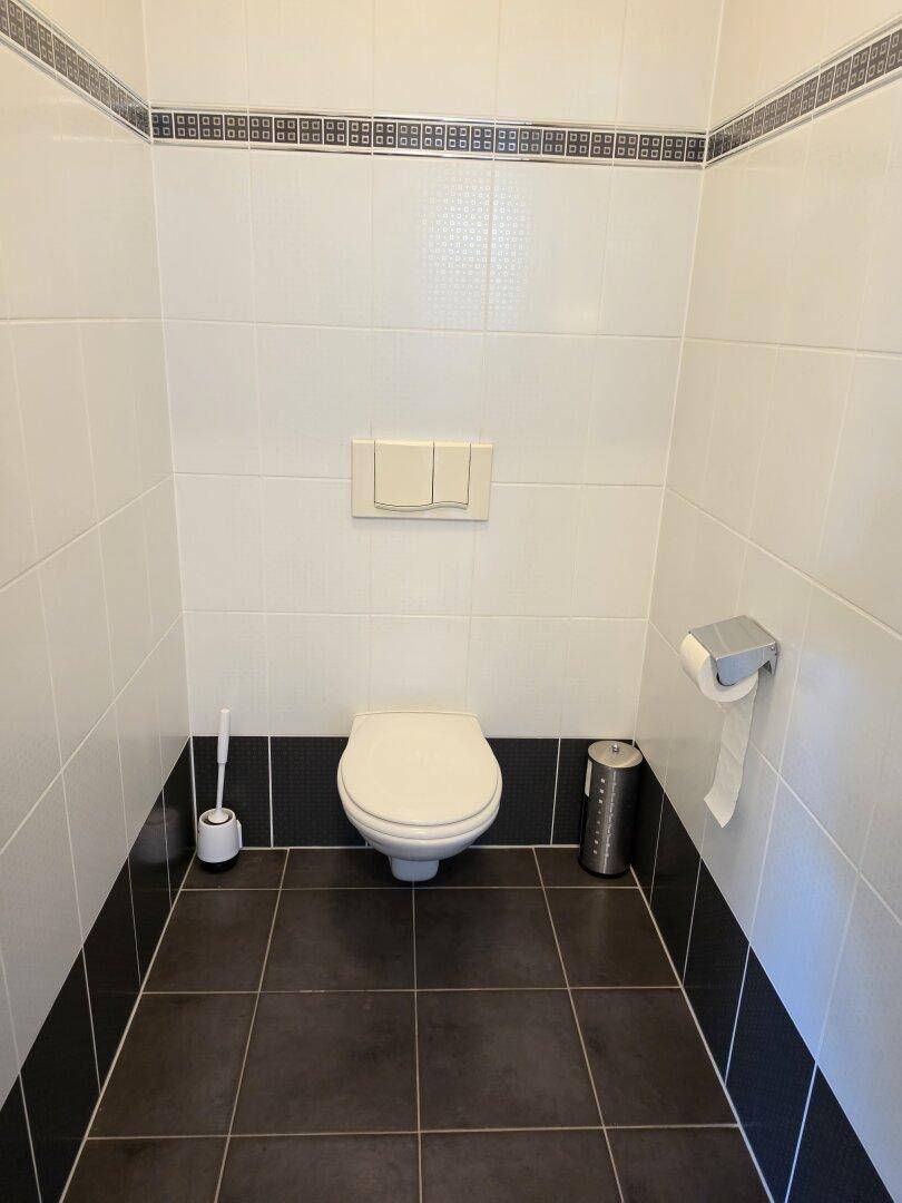 Gästetoilette mit wandhängendem WC und weiß-schwarz gefliesten Wänden und dunklem Boden.
