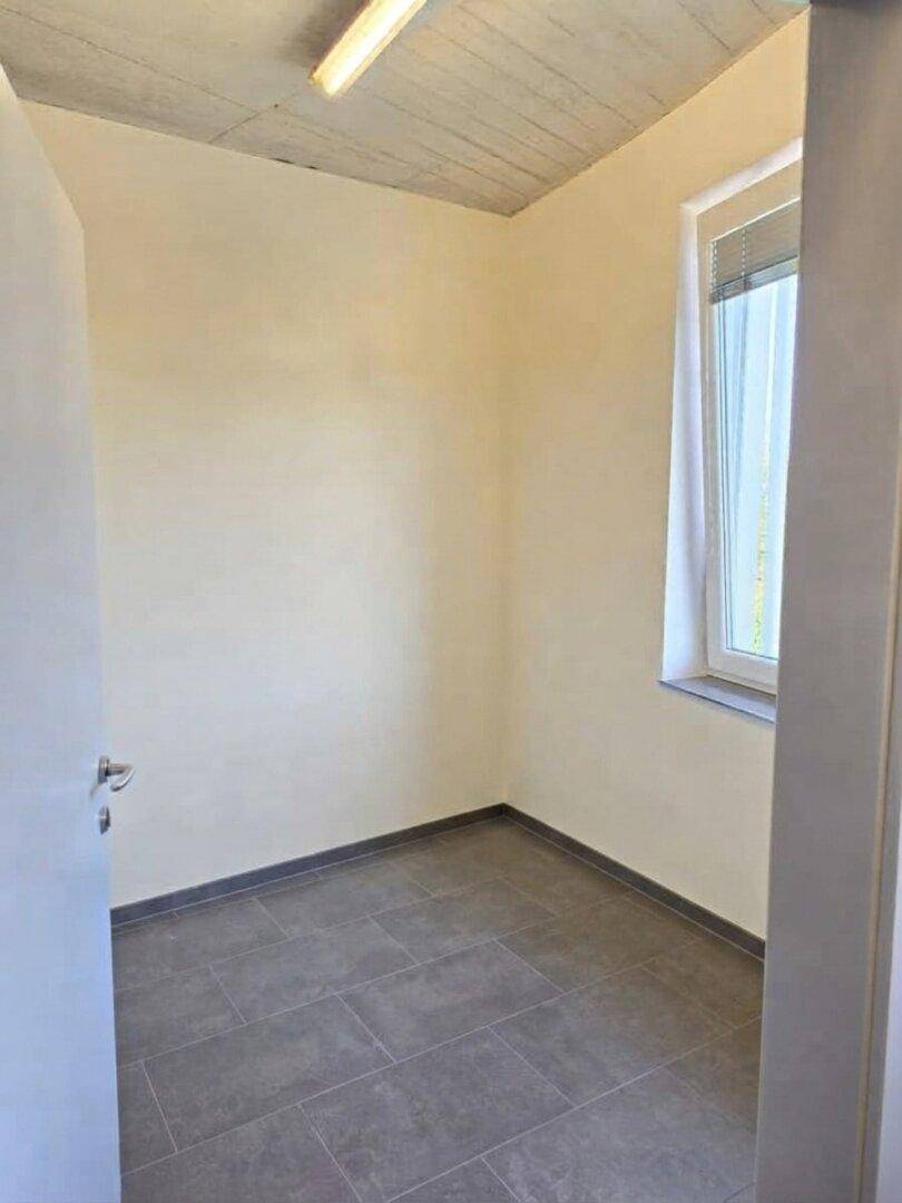 Kleiner, leerer Büroraum mit hellen Wänden, Fliesenboden und einem Fenster für Tageslicht.