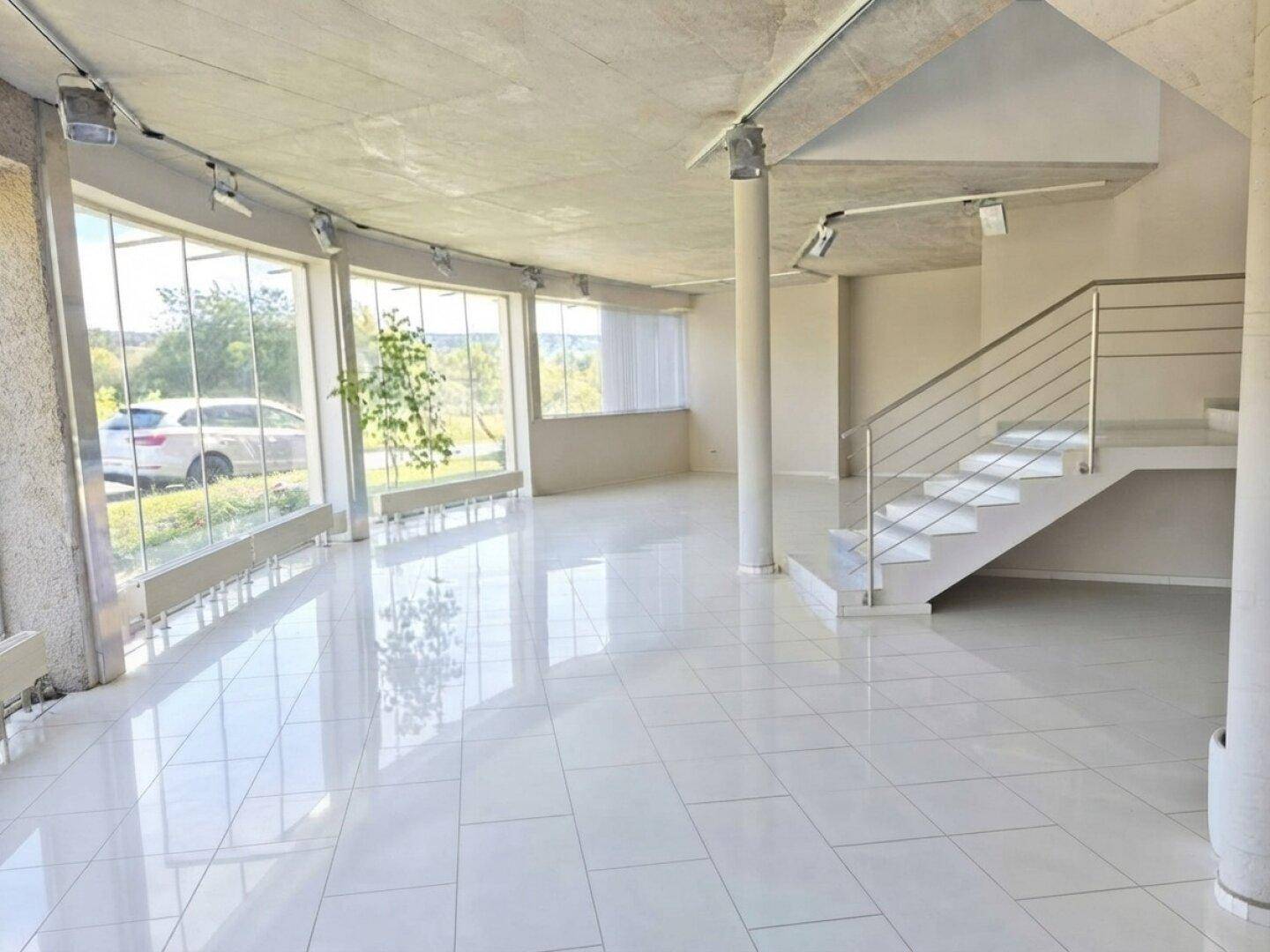 Heller, offener Gewerberaum mit großen Fenstern, glänzenden Fliesen und einer modernen Treppe.