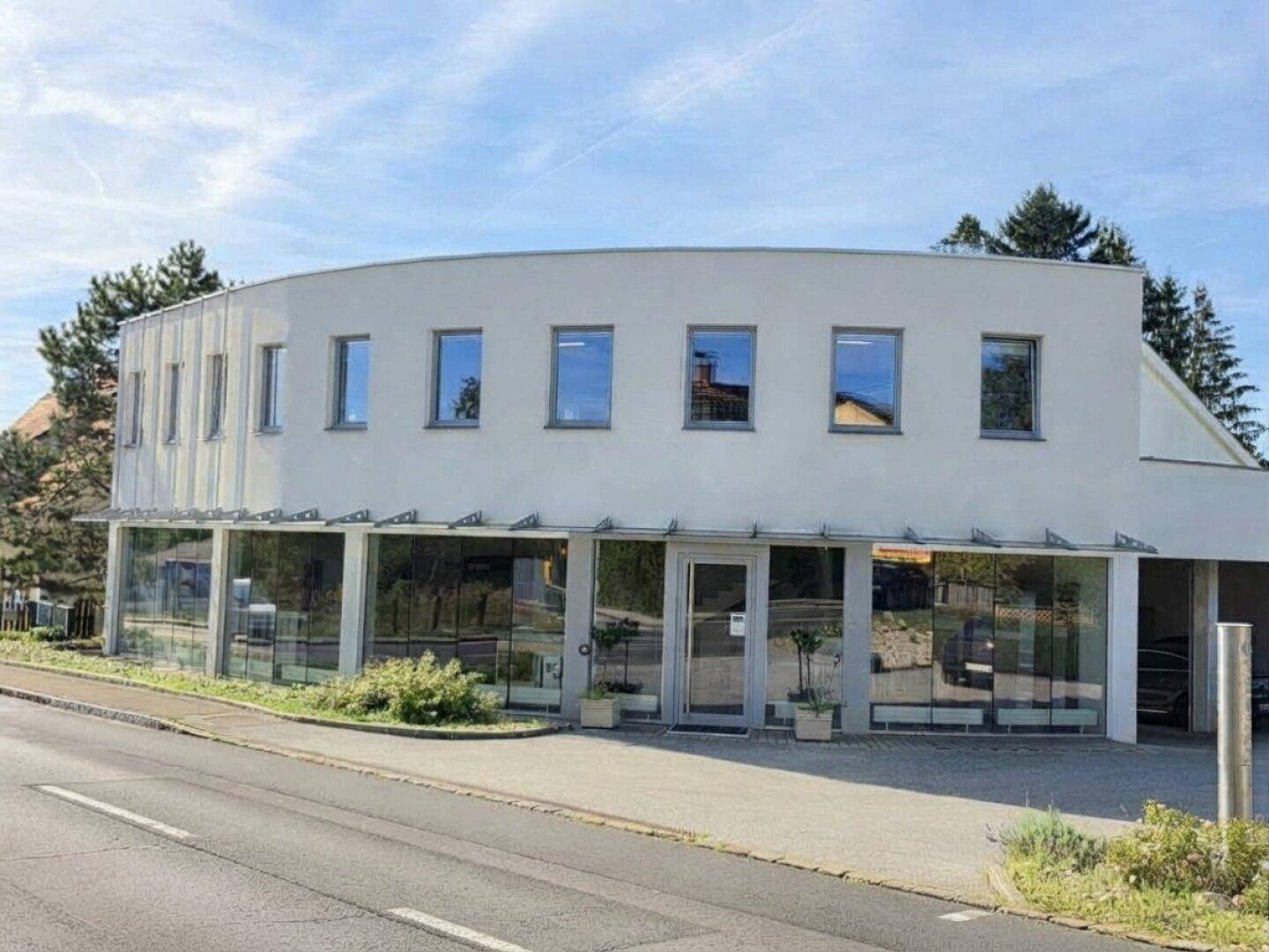 Moderne Geschäftsfassade mit geschwungener Architektur, großen Schaufenstern und Obergeschossfenstern.