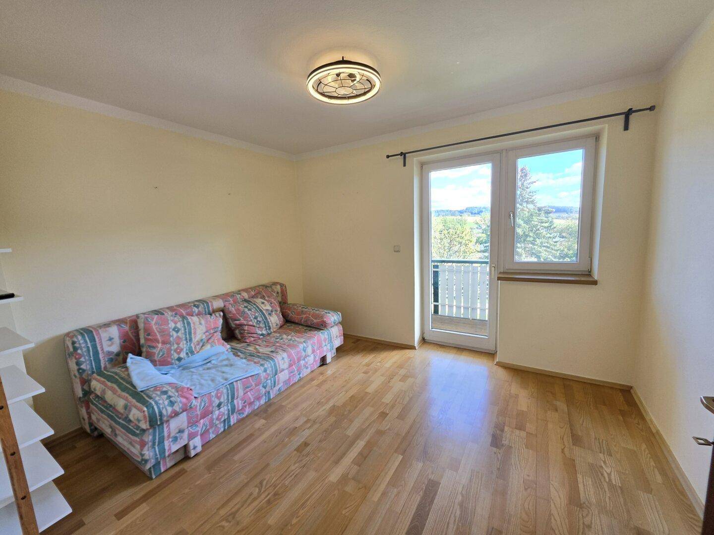 Schlafzimmer mit Holzboden, Sofa und Zugang zu einem französischen Balkon.