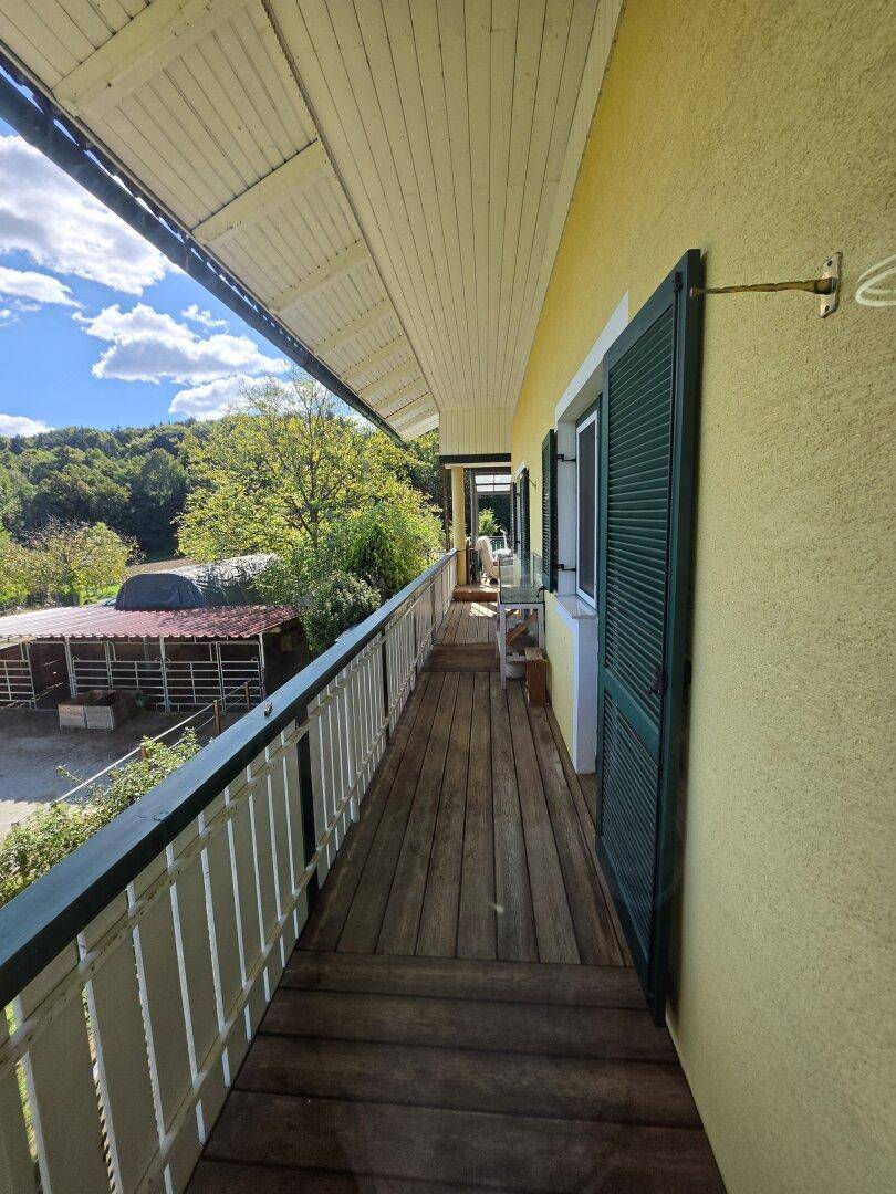 Langer Balkon mit Holzboden, weißem Geländer und Blick auf die Umgebung.