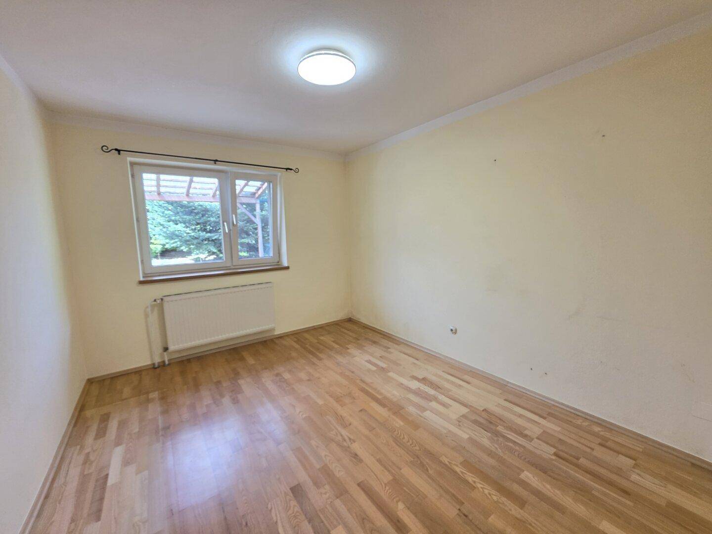 Helles Schlafzimmer mit Holzboden, weiß gestrichenen Wänden und Fenster.