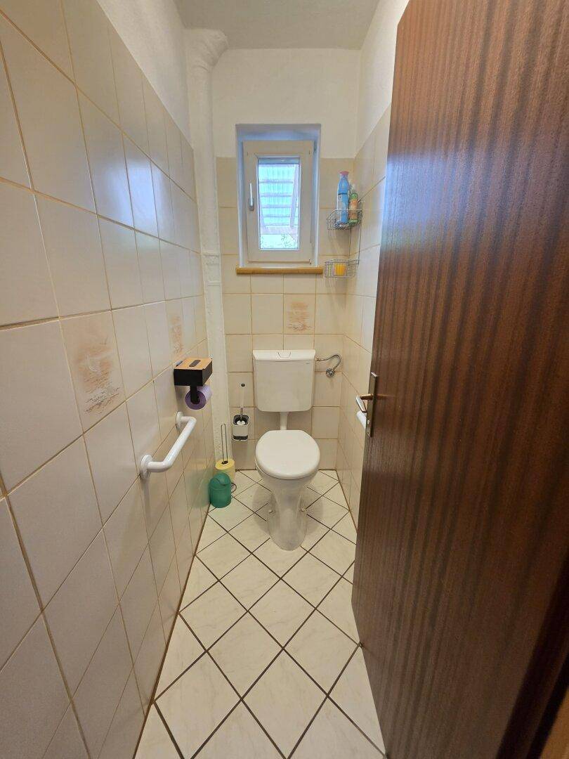 Kleines WC mit Fliesenboden, Toilette und Haltegriff an der Wand.