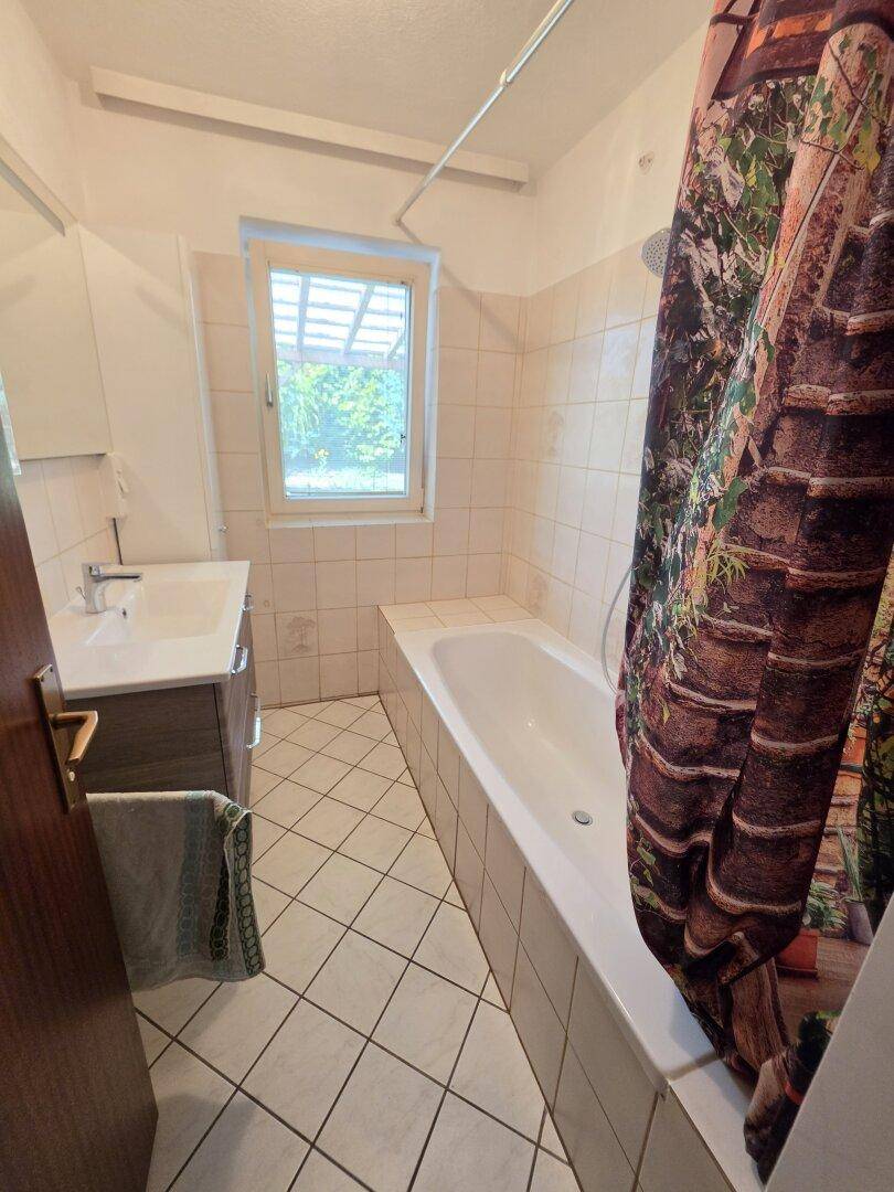 Badezimmer mit Badewanne, Waschbecken und Fenster, gefliesten Wänden und Boden.