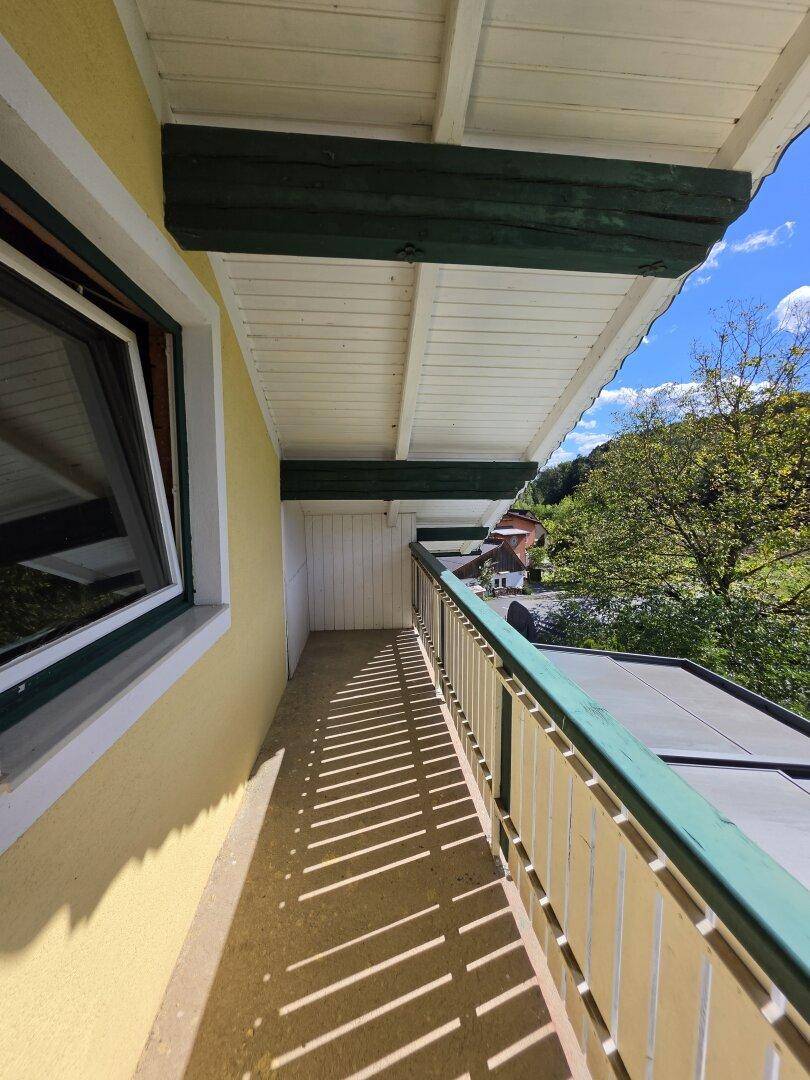 Schmaler Balkon mit Holzboden und Geländer, bietet einen schönen Blick ins Grüne.