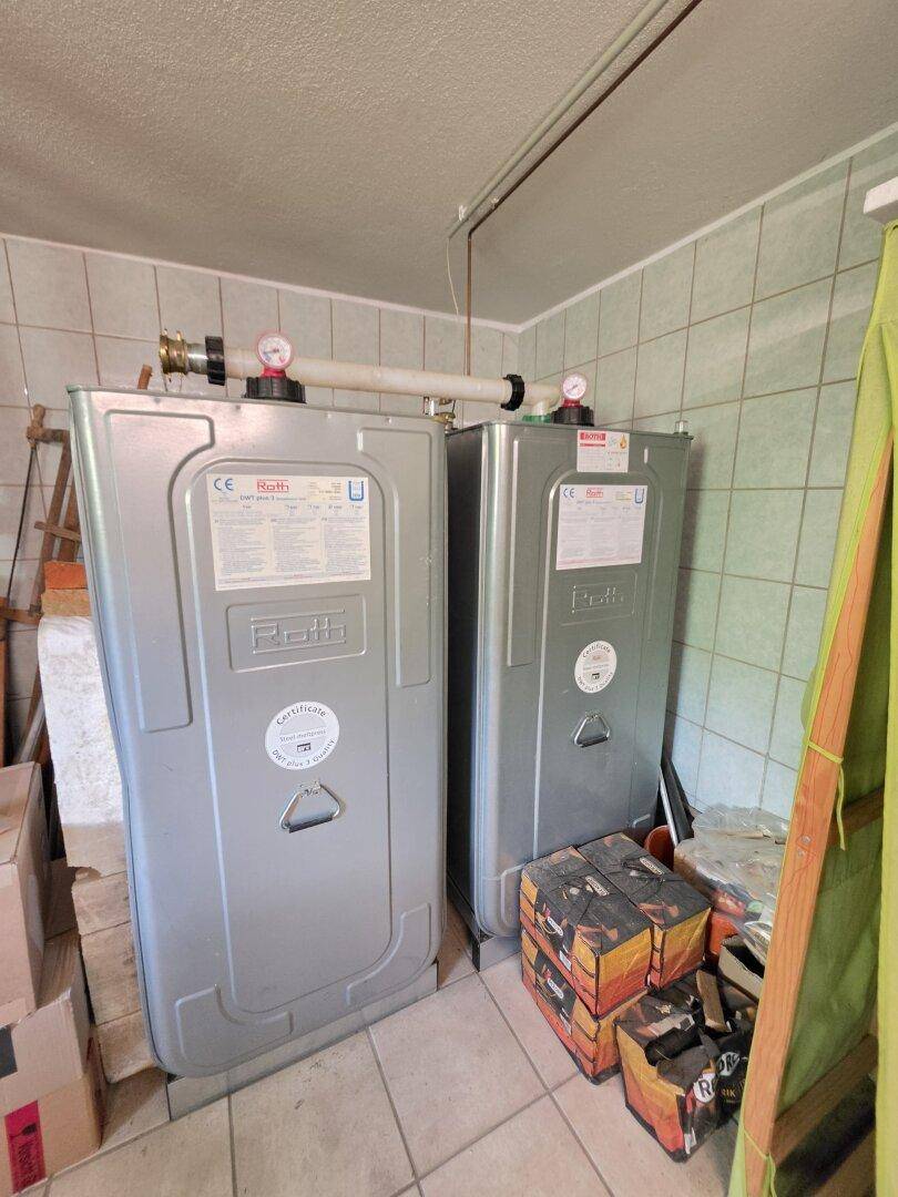 Kellerraum mit zwei großen Warmwasserspeichern und Fliesenboden, dient als Technikbereich.
