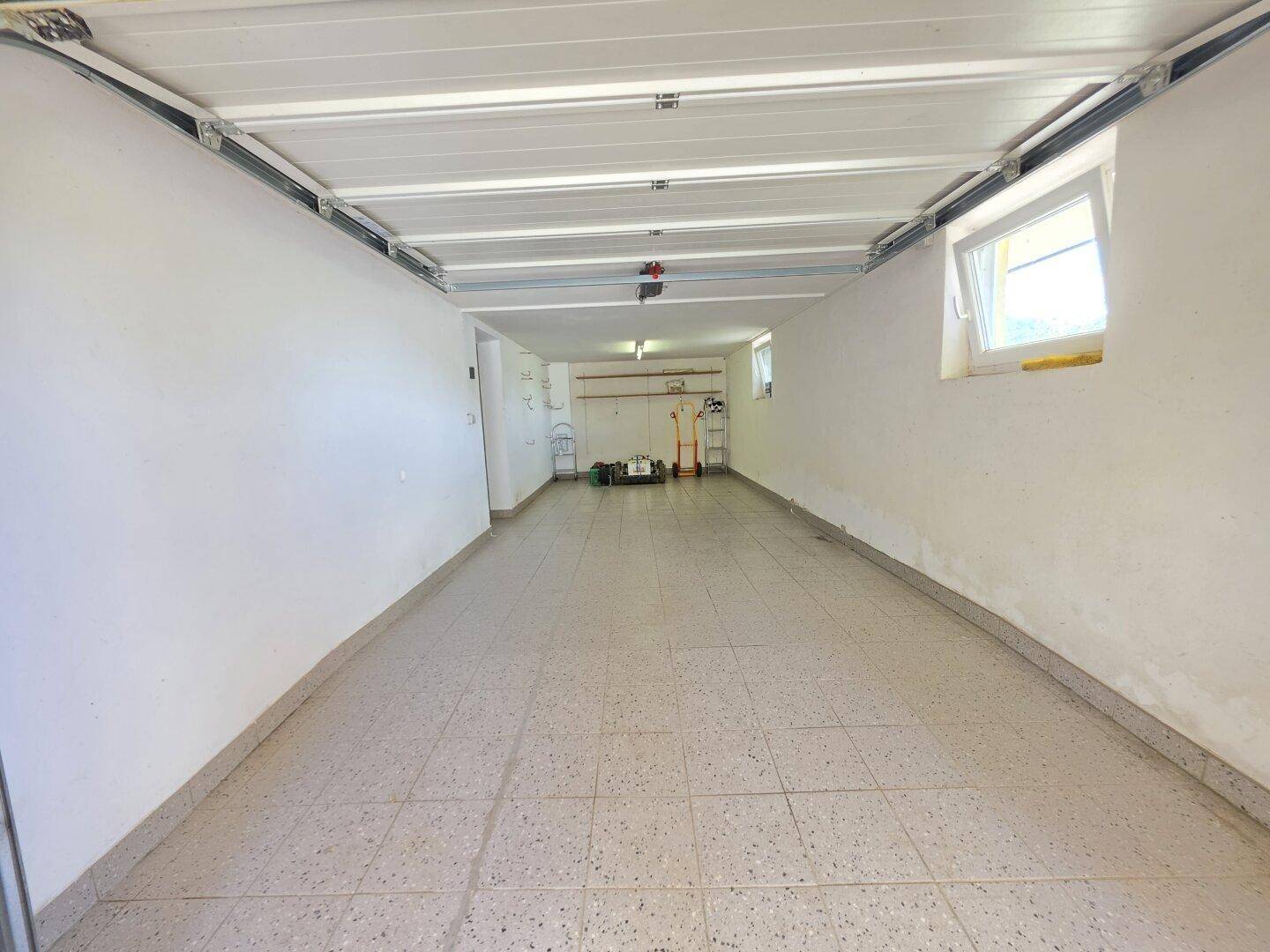 Lange Garage mit Fliesenboden und Fenstern, bietet Platz für mehrere Fahrzeuge.