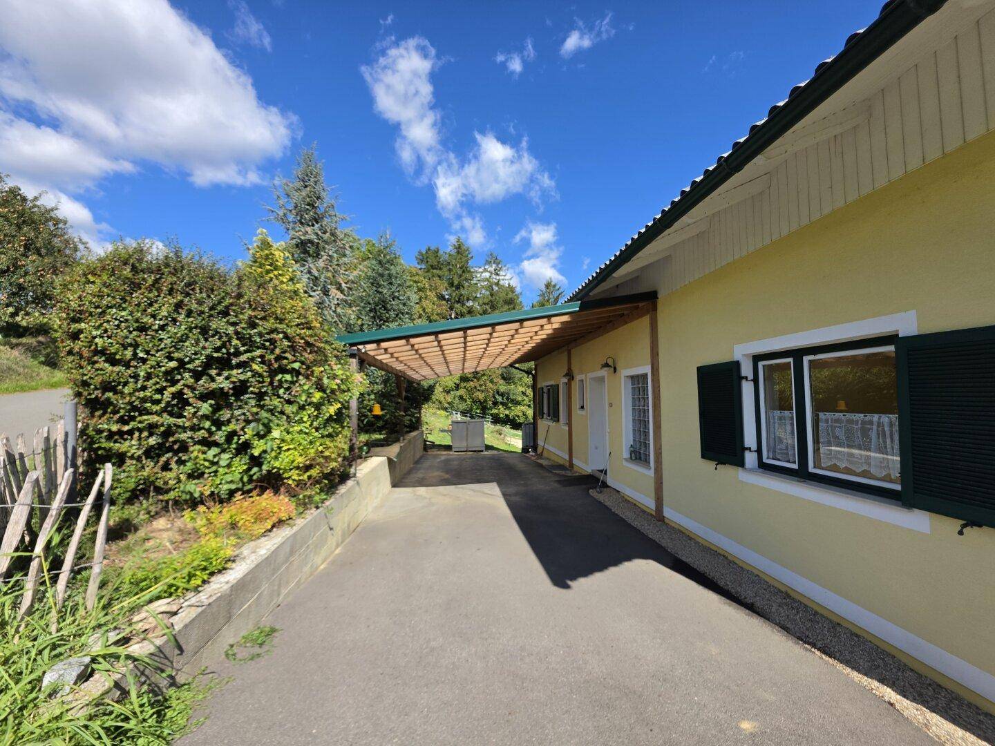 Seitenansicht des Hauses mit einem überdachten Carport und einer Zufahrt.