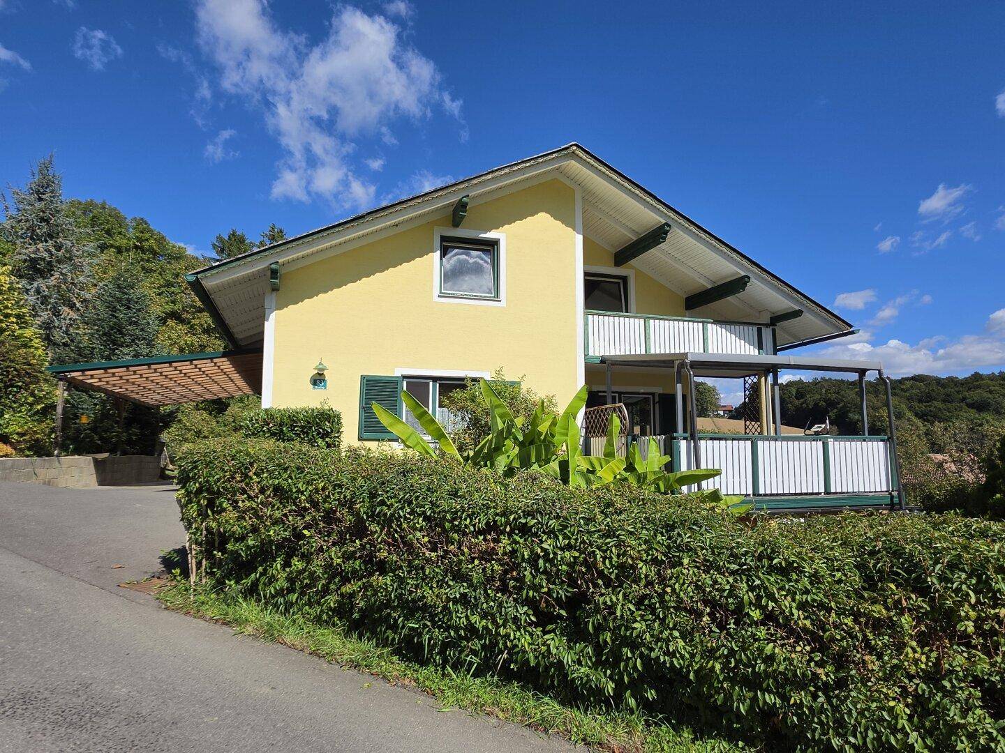 Charmantes gelbes Haus mit Balkon und grüner Hecke, eingebettet in die Landschaft.