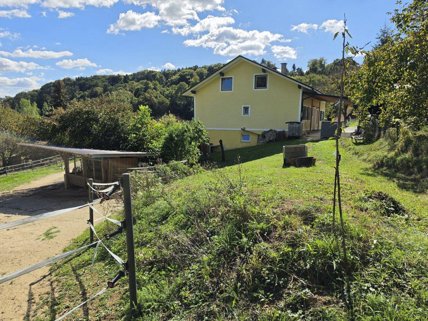 Seitenansicht des gelben Hauses von einem Feld aus, mit einem Unterstand im Vordergrund.