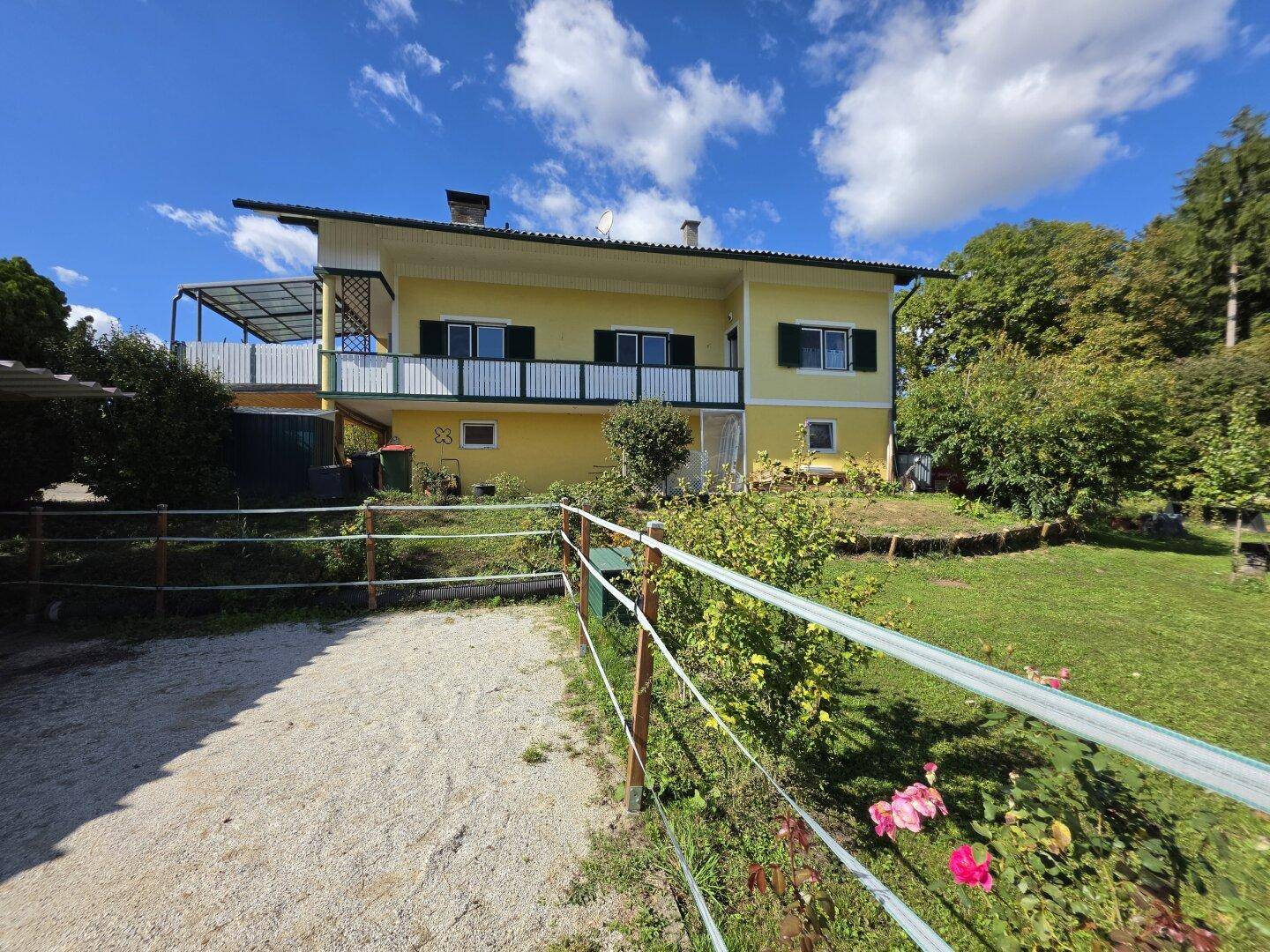 Ansicht des gelben Wohnhauses mit Balkon und Gartenbereich unter strahlend blauem Himmel.