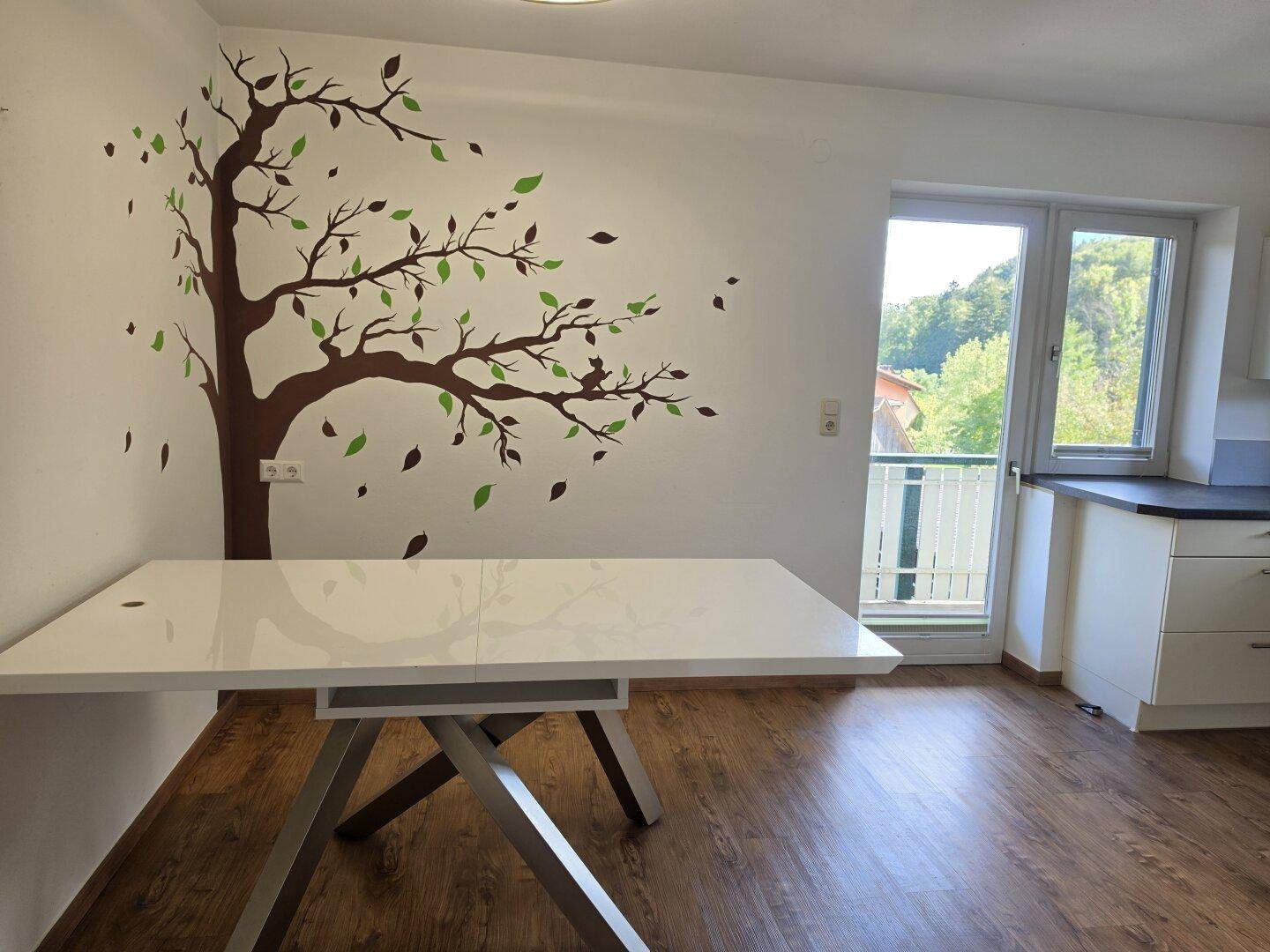 Essbereich mit modernem weißen Tisch und dekorativer Baumwandmalerei.