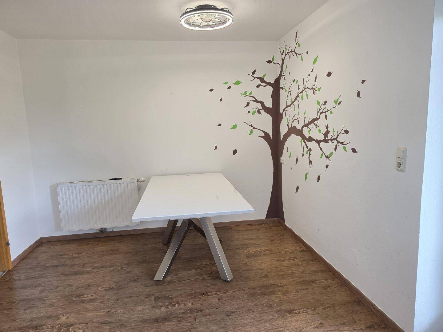 Essbereich mit modernem Tisch, Laminatboden und dekorativem Baumwandtattoo.