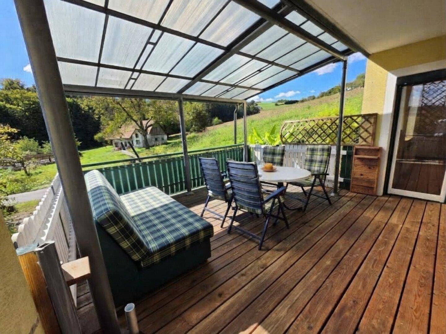 Überdachte Terrasse mit Holzboden, Gartenmöbeln und weitem Blick ins Grüne.