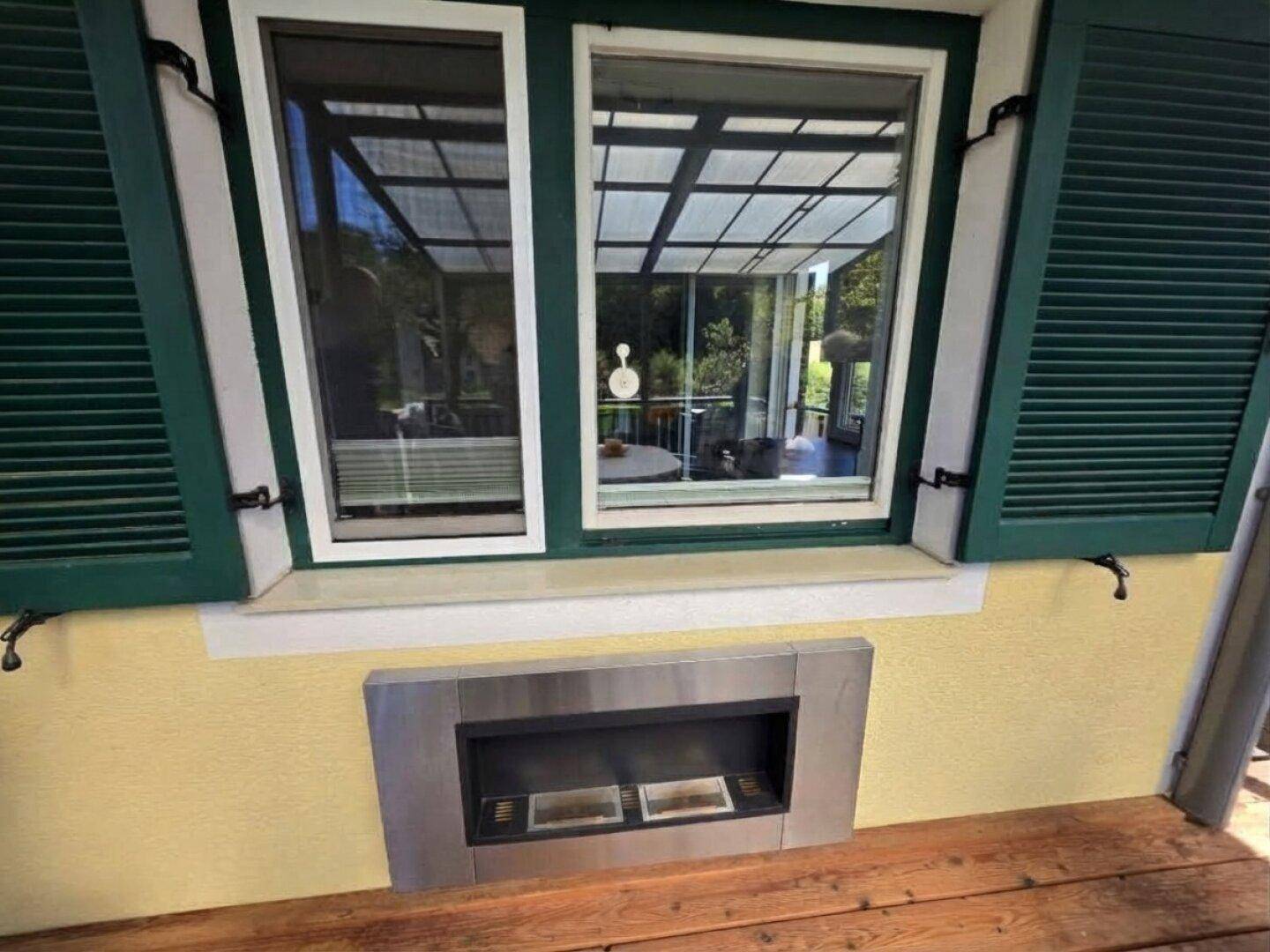 Fenster mit Blick auf die überdachte Terrasse und einen modernen Außenkamin.