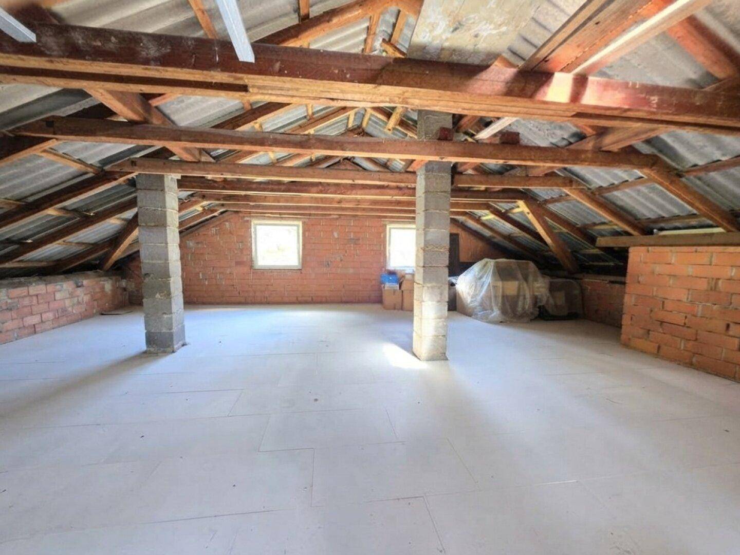 Geräumiger Dachboden mit sichtbaren Holzbalken und Ziegelwänden, bereit zum Ausbau.