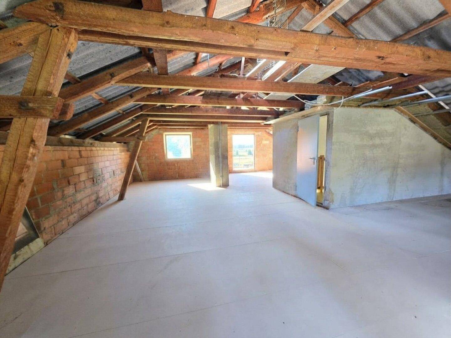 Großer Dachbodenbereich mit Holzbalken, Ziegelwänden und Potenzial für Wohnraum.