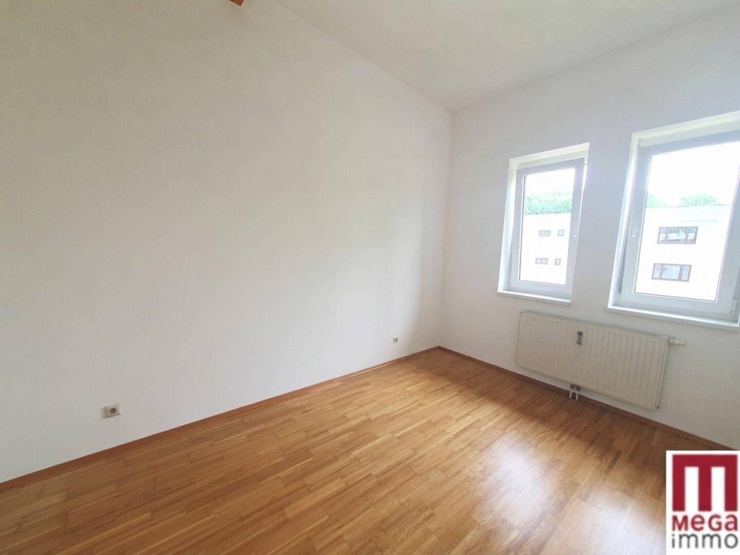 Helles Schlafzimmer mit Parkettboden und Heizkörper unter den Fenstern.
